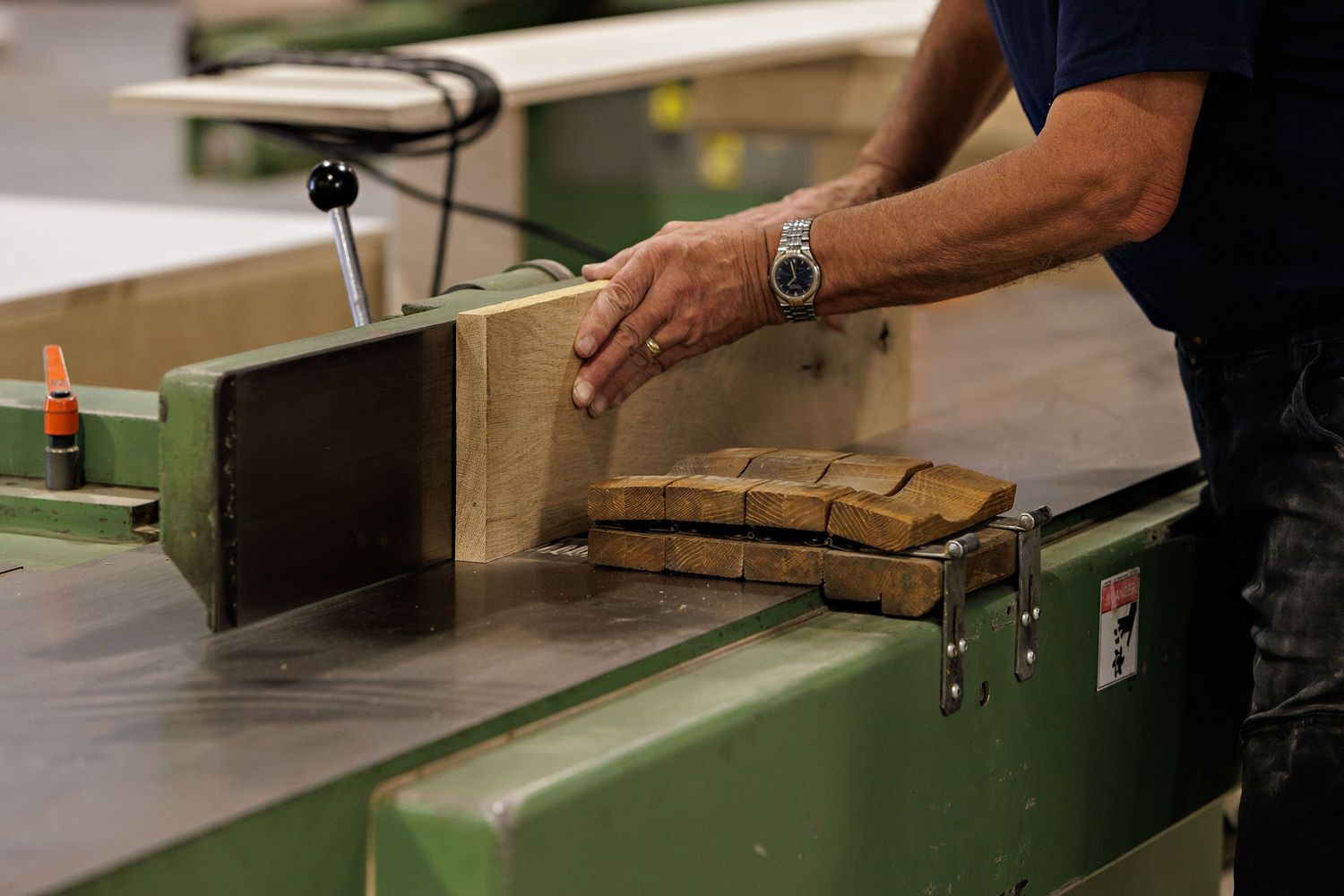 A woodworker guides lumber through an industrial jointer machine in a workshop.