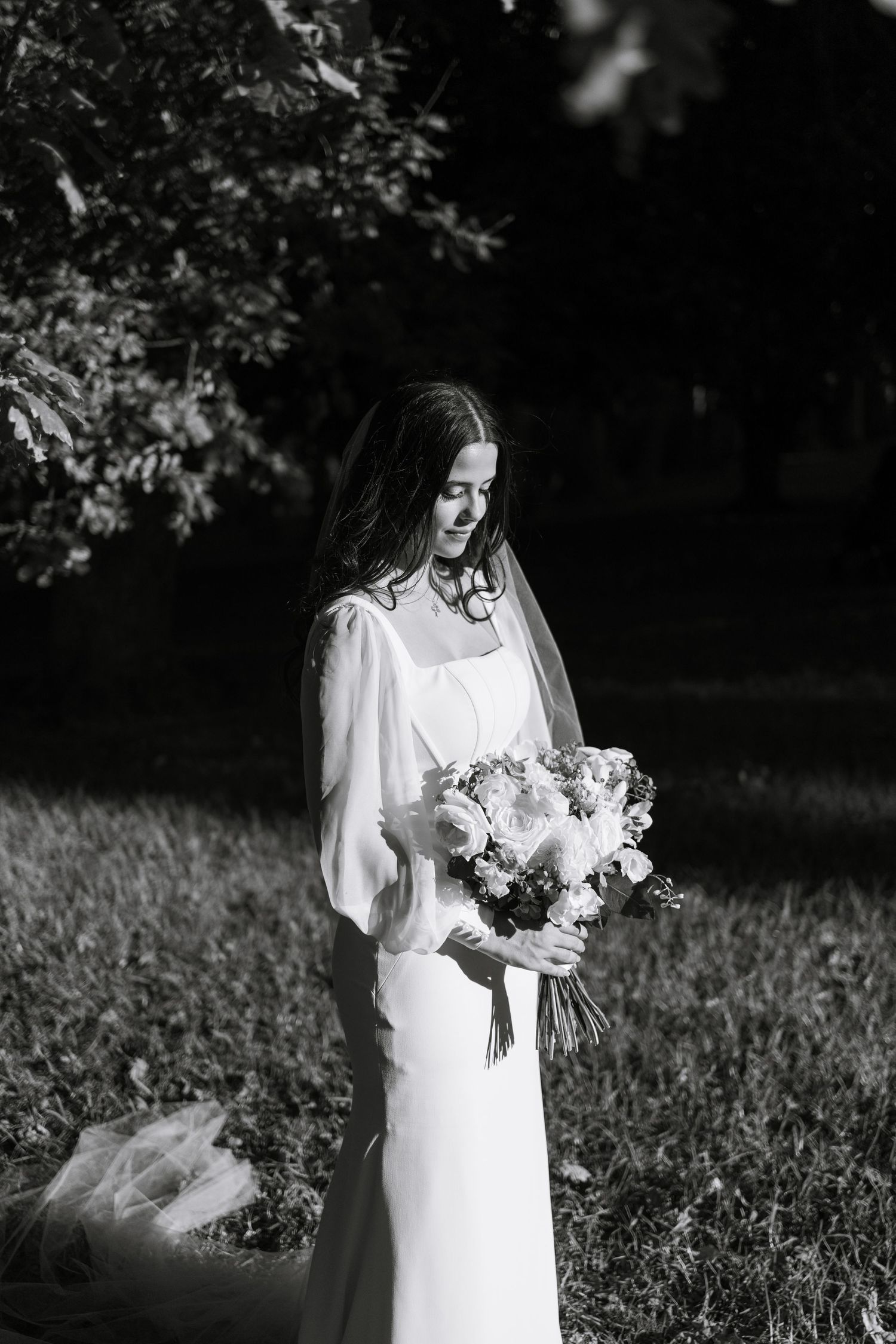 Elegant white wedding dress with long sleeves photographed in dramatic black and white outdoor setting.