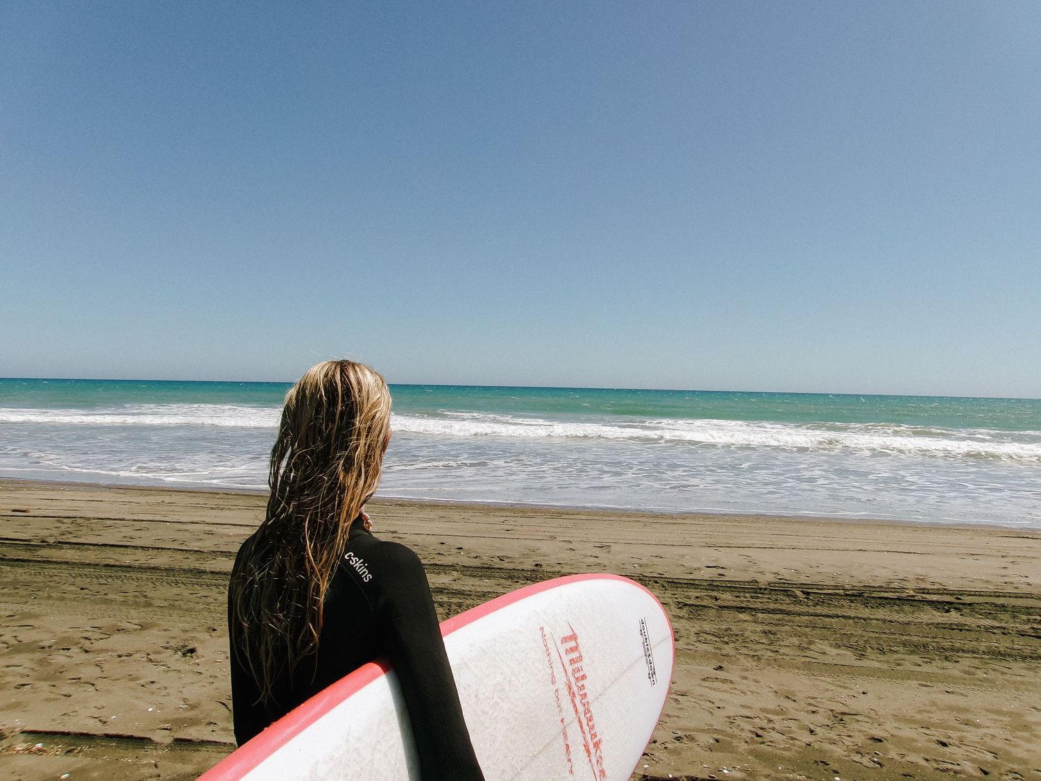 Scenic beach landscape with surfboard and ocean waves under clear blue sky.