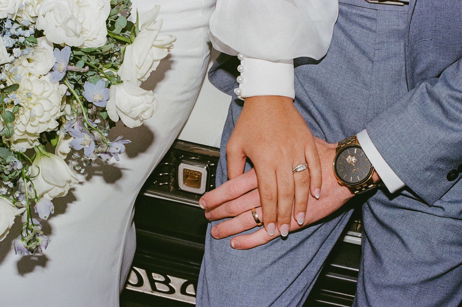 Close-up detail of wedding rings and hands against a floral background.