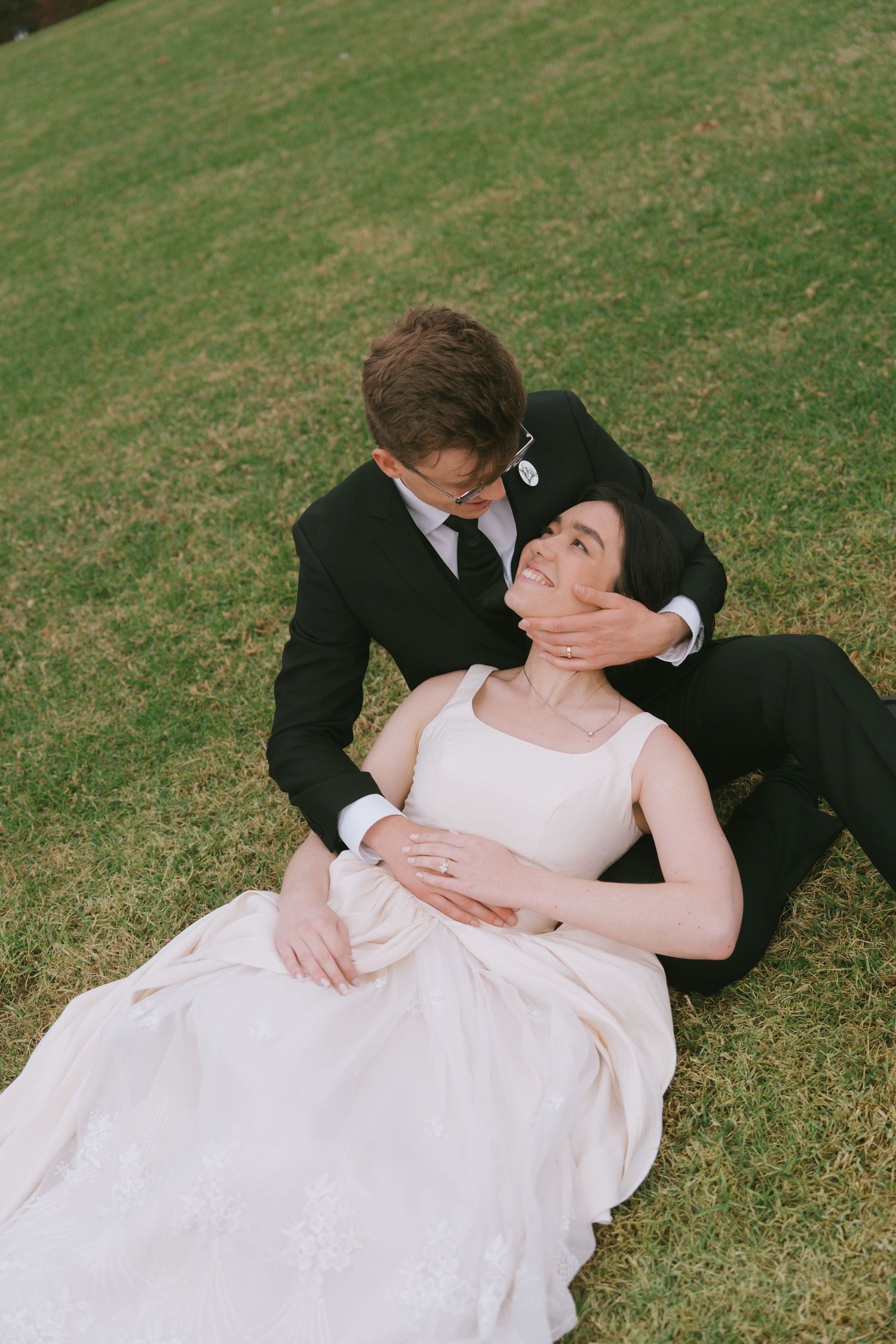 A couple in formal wedding attire sharing intimate moments on a grassy slope.