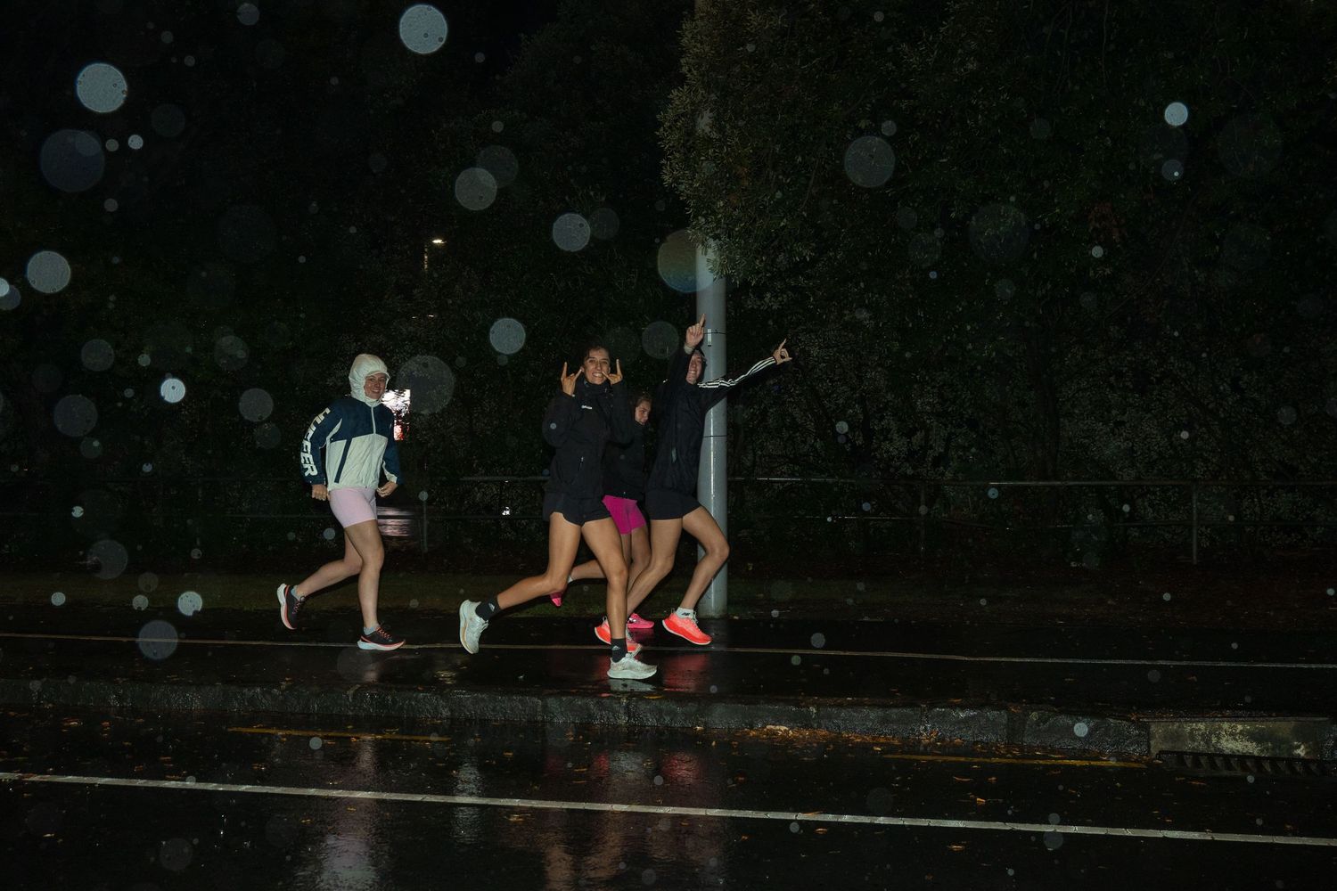 Three people running in the rain at night with light reflections visible.