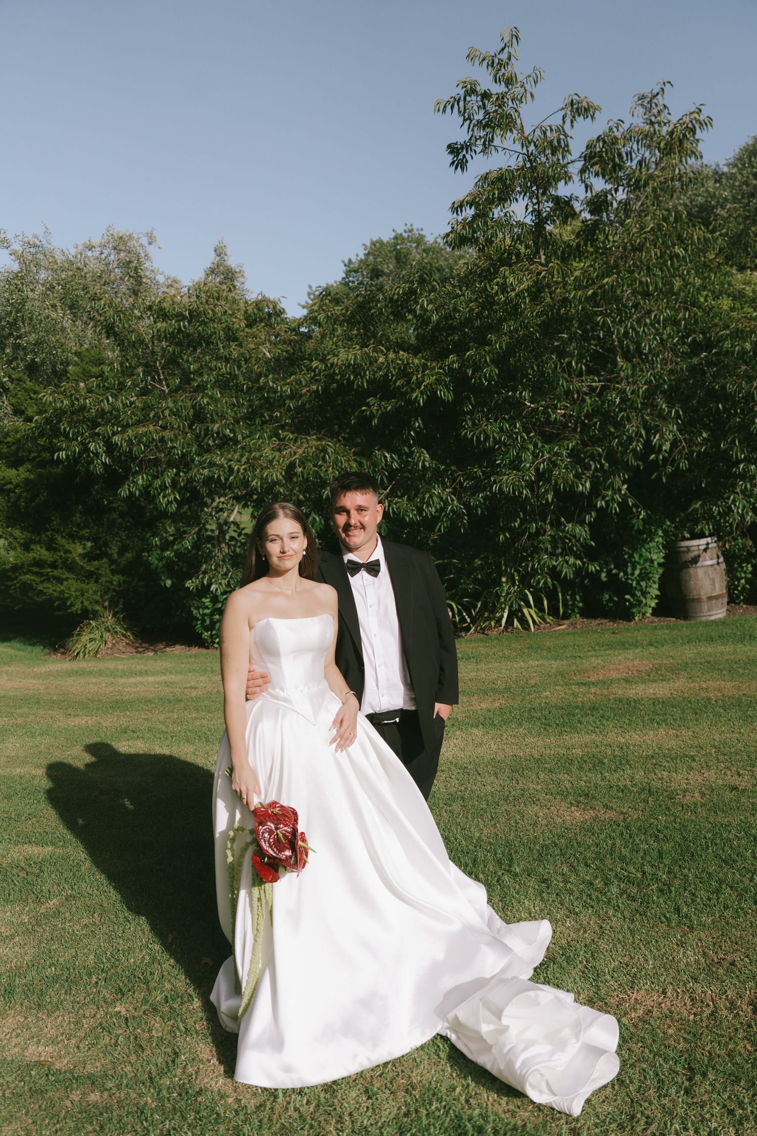 Bride in white dress and groom in tuxedo posing for photos in a garden setting.
