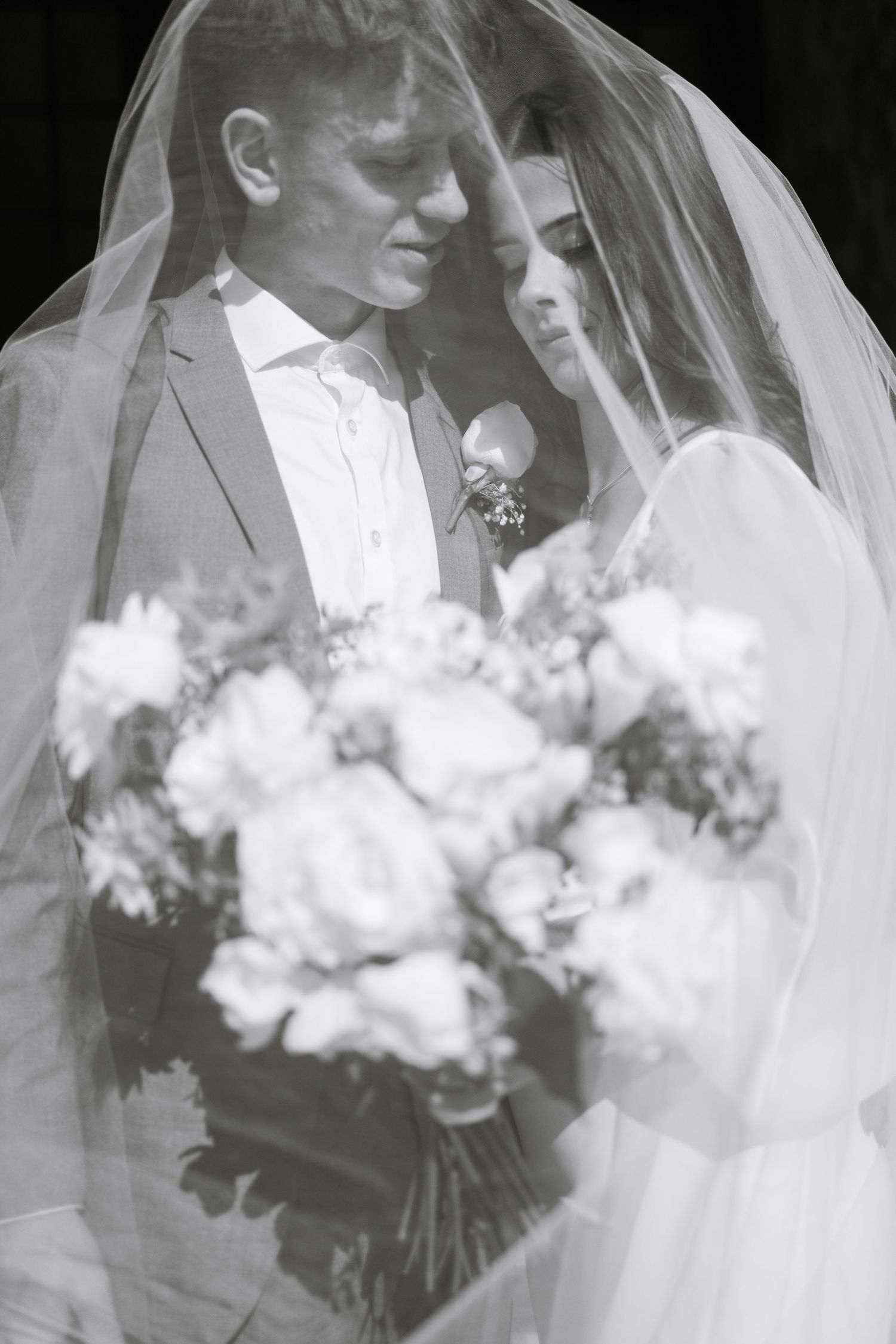 Black and white wedding portrait with white floral bouquet in the foreground.