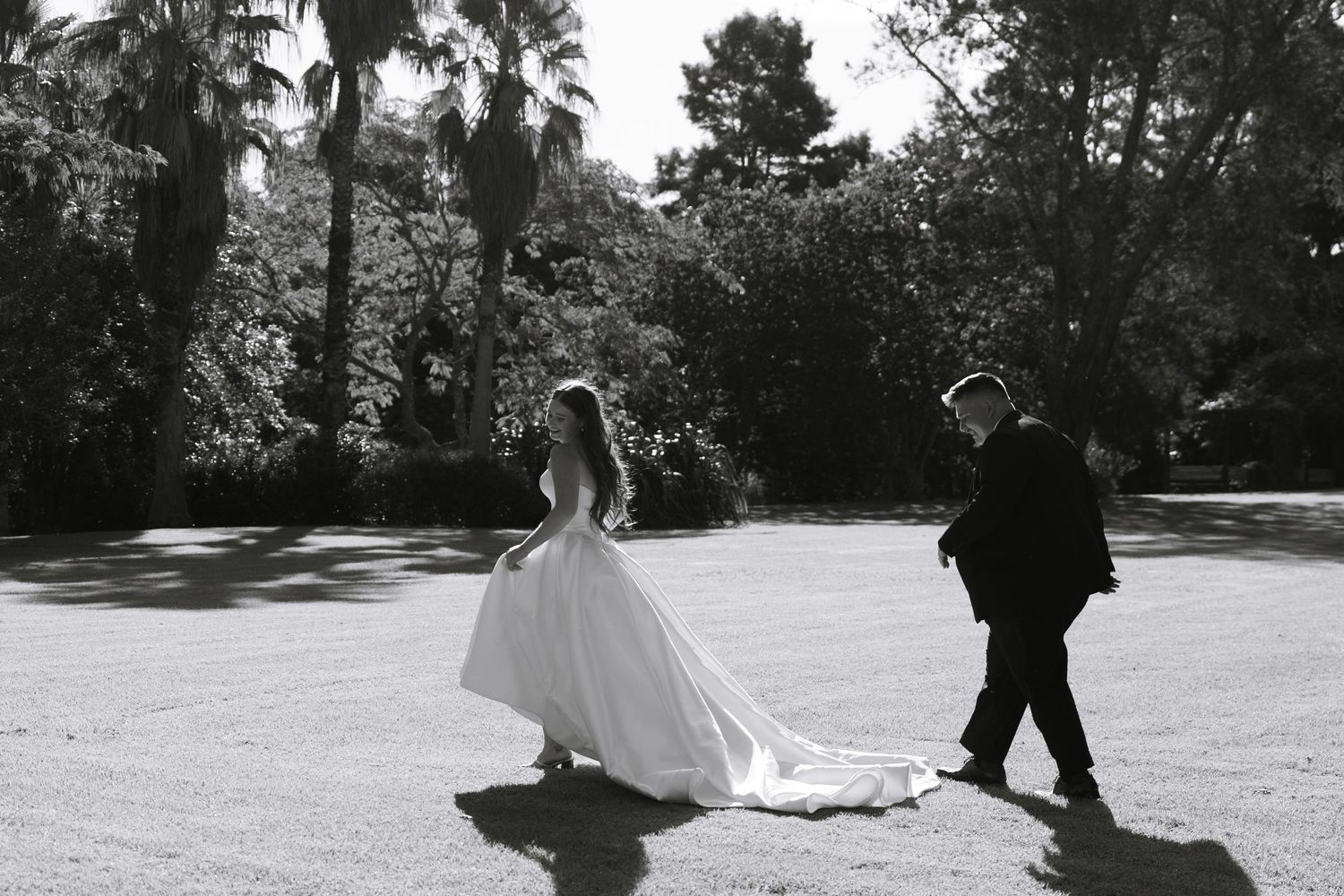 Wedding couple walking through a sunlit garden path in black and white.