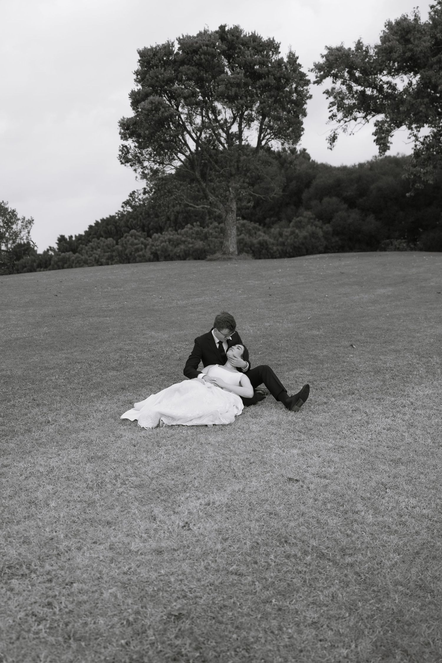 Wedding couple lies together on grassy hill in artistic black and white photo sequence.