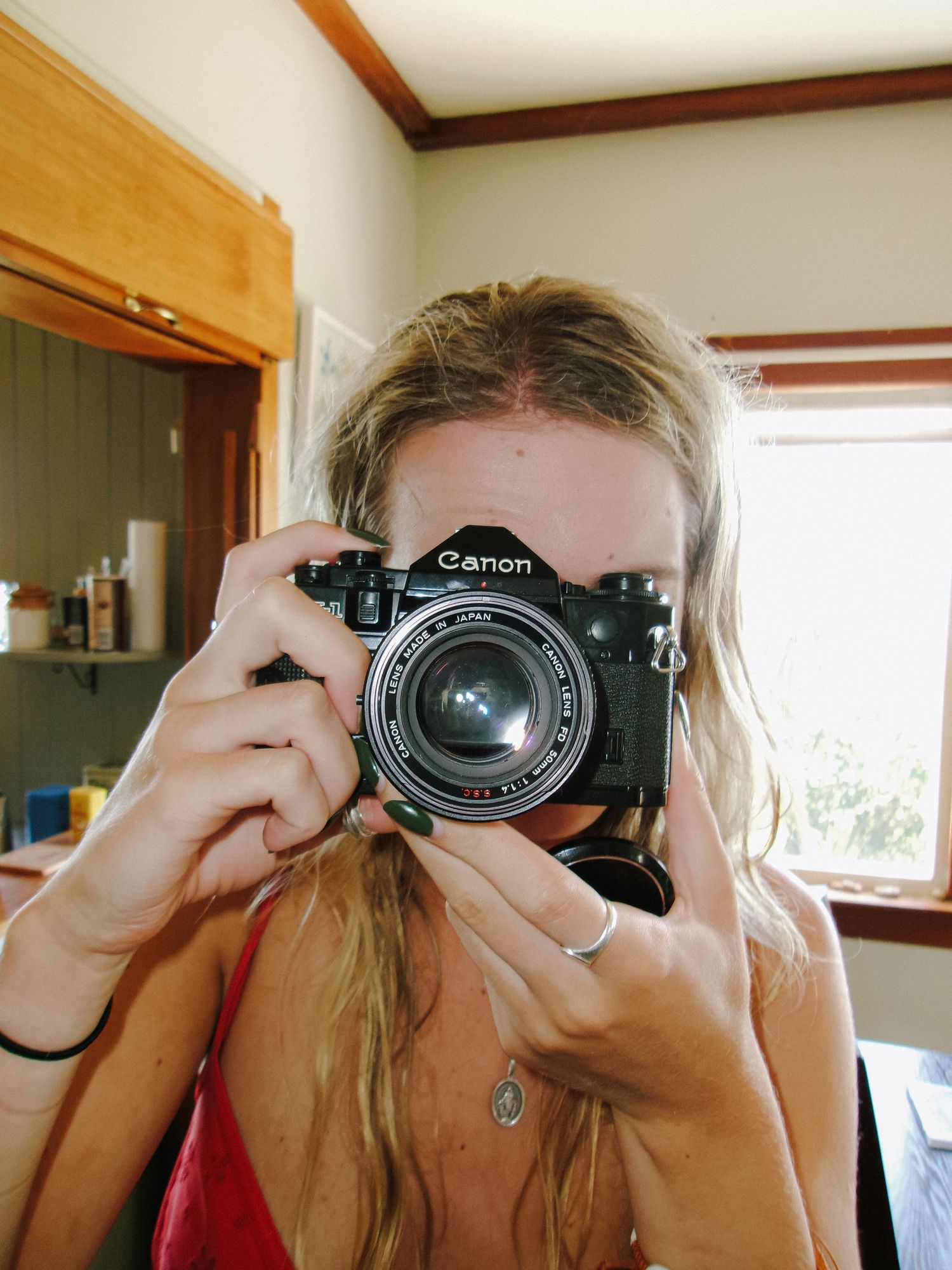 Person holding vintage Canon camera for self-portrait in indoor setting.
