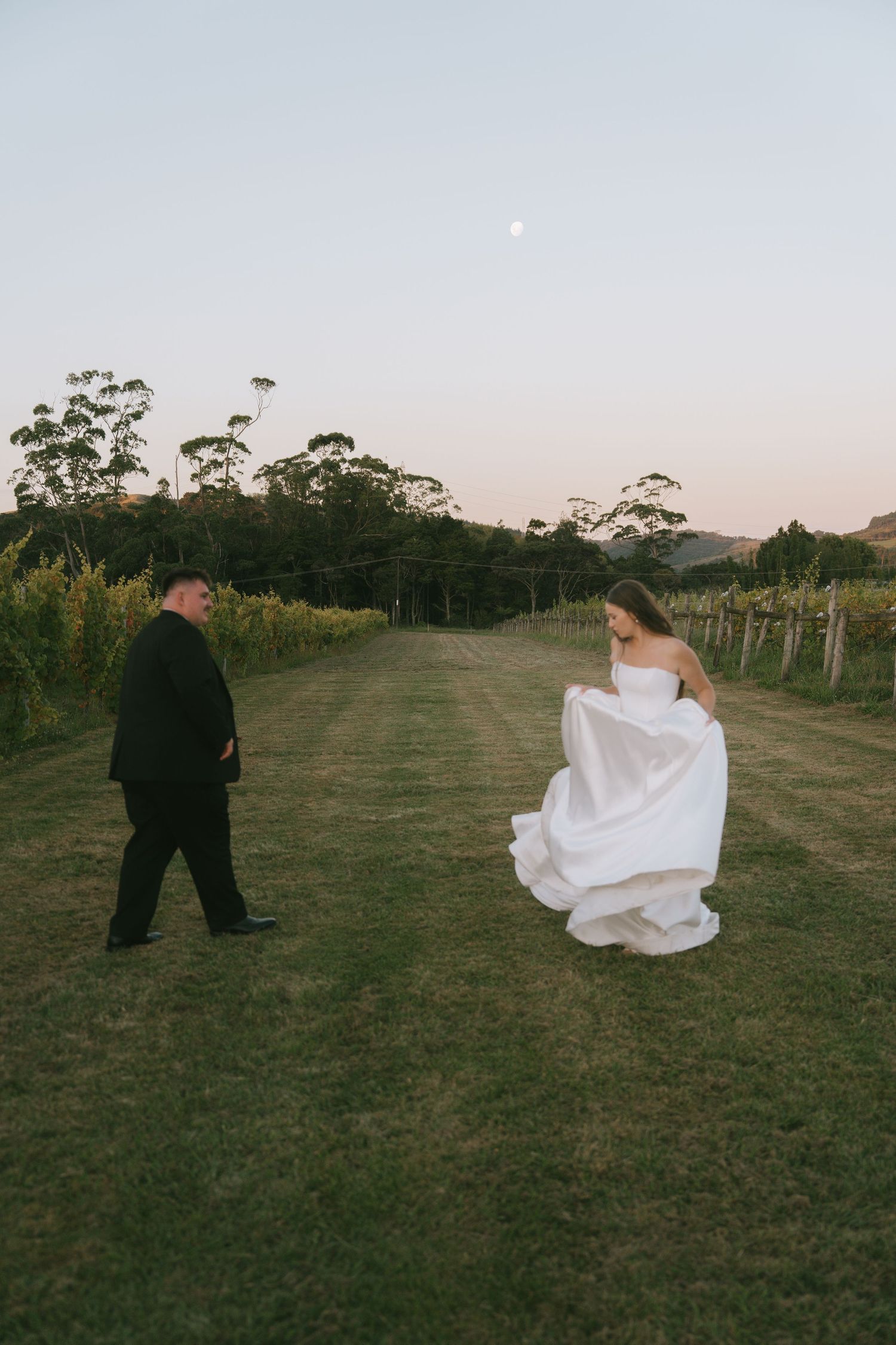 Wedding couple running playfully through a grassy field at dusk.