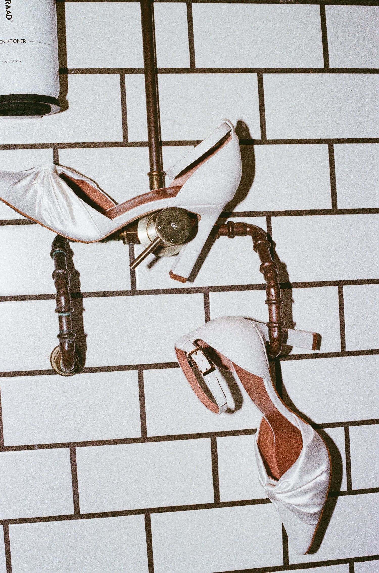 White wedding shoes arranged artistically against a white tiled wall background.