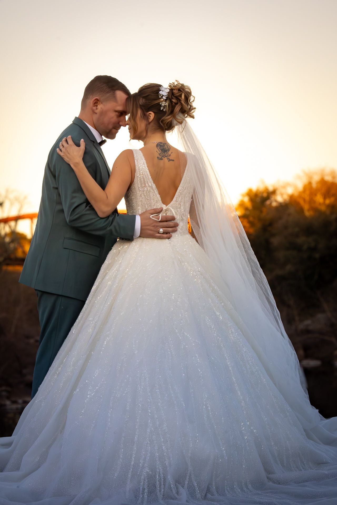 A romantic sunset wedding photo showing a couple embracing, with the bride in a flowing white gown with long veil.