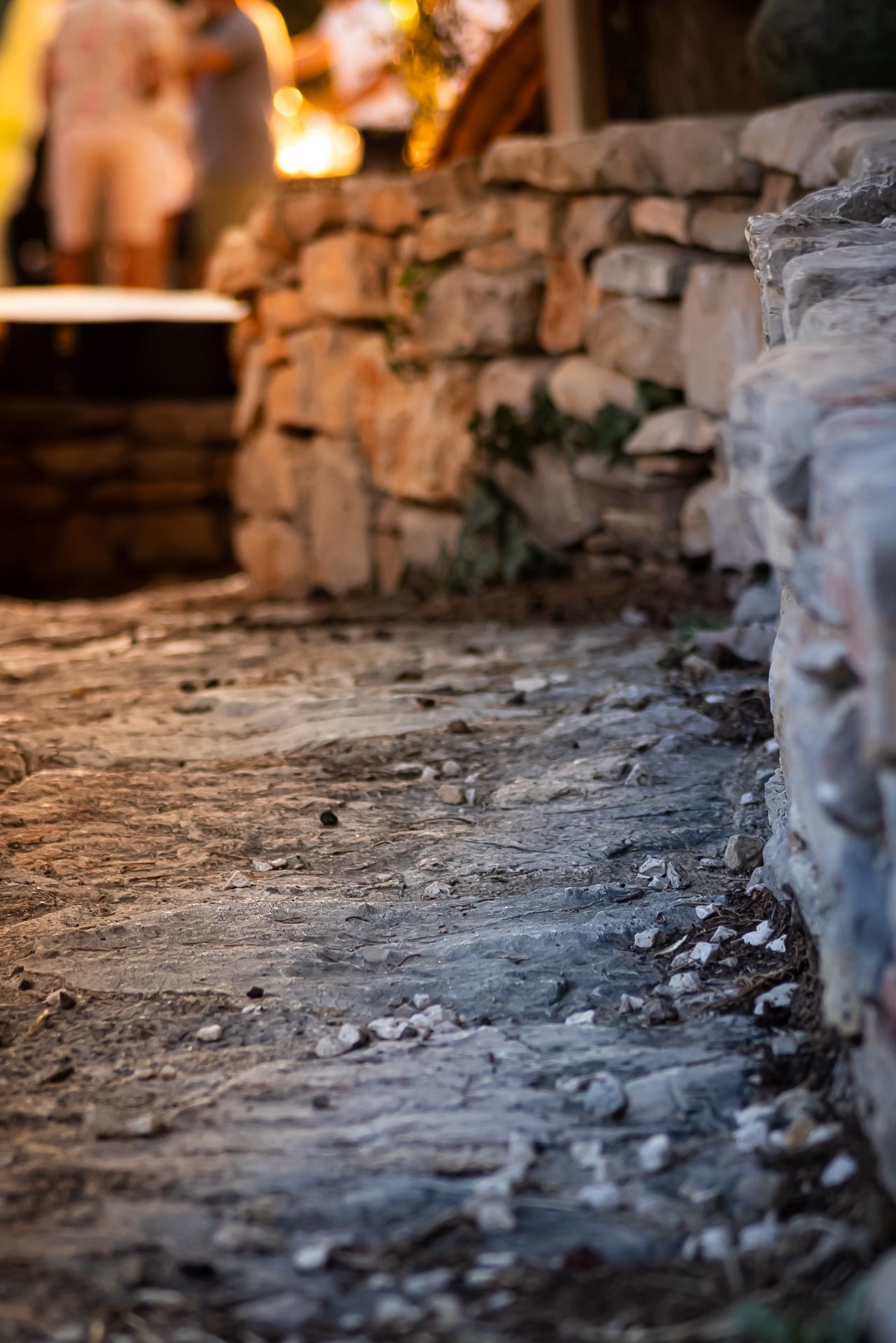 Close-up of rustic stone pathway with blurred stone wall and warm lights in background.