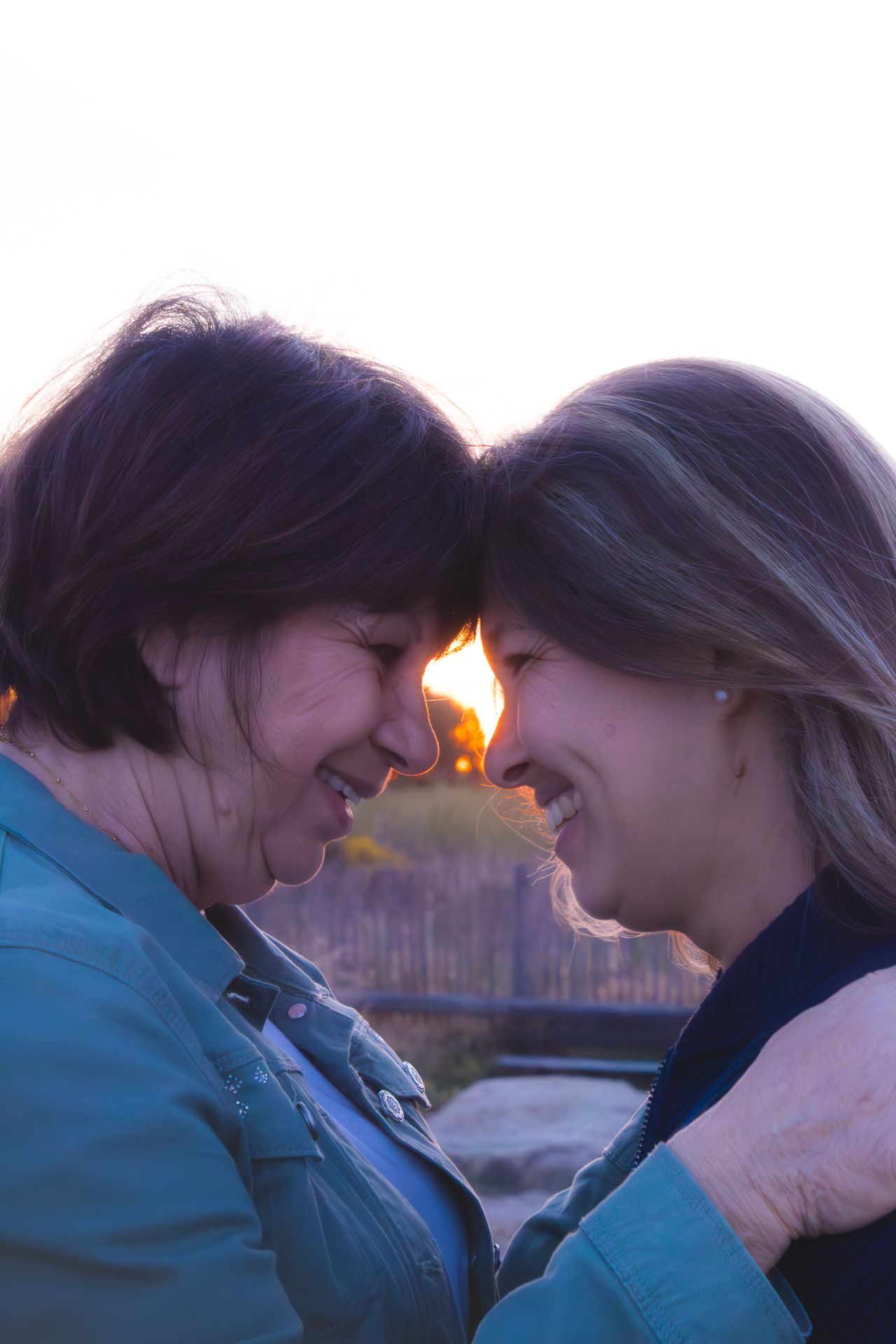 Two women smiling and touching foreheads at sunset, sharing a joyful and intimate moment outdoors.