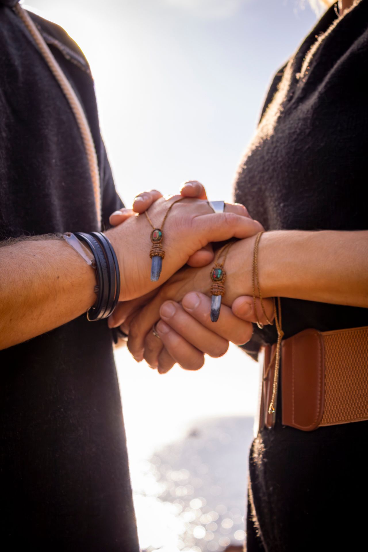 Close-up view of hands holding each other in silhouette against a bright sky during sunset.