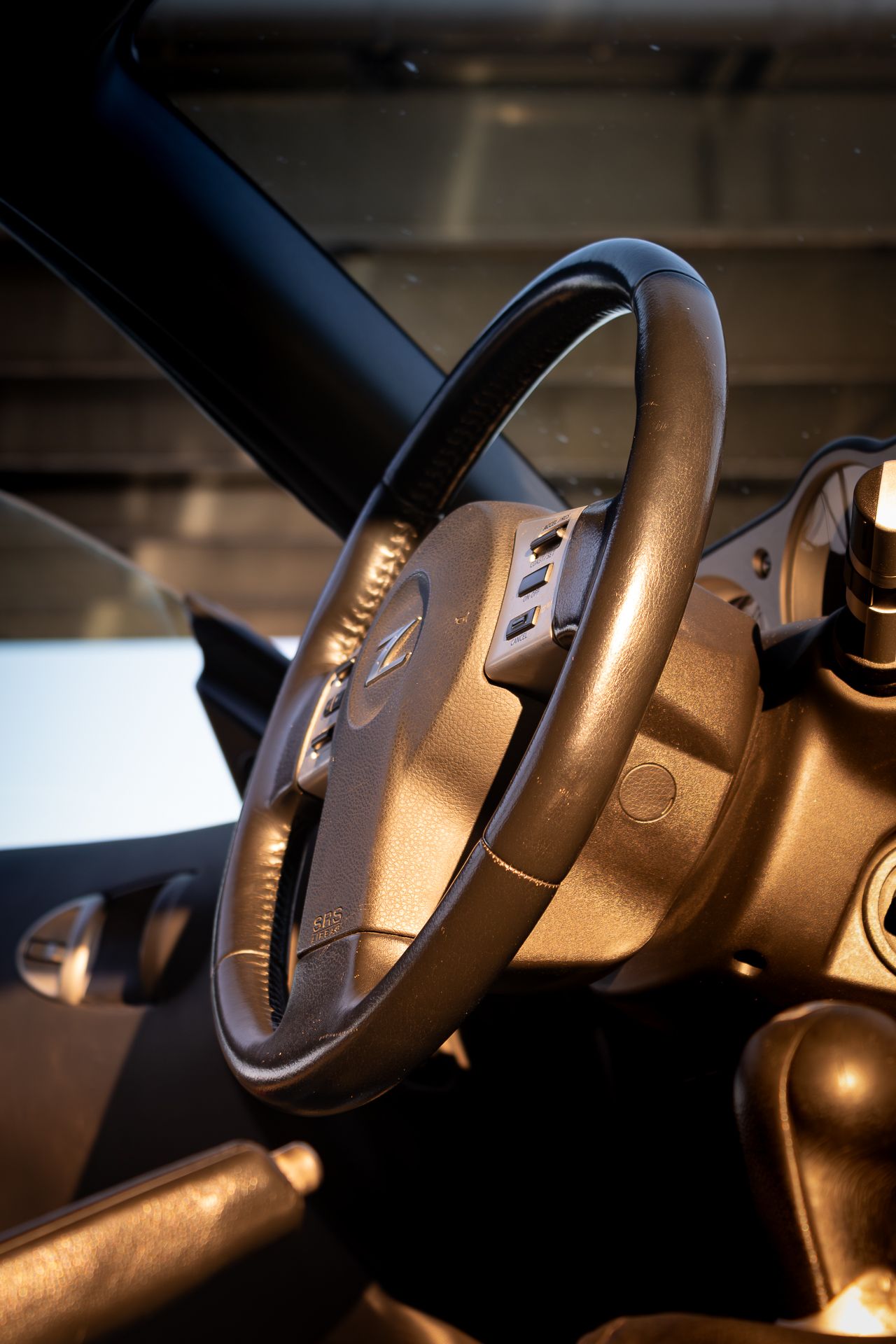 Close-up view of a modern car steering wheel with metallic accents illuminated by warm interior lighting.