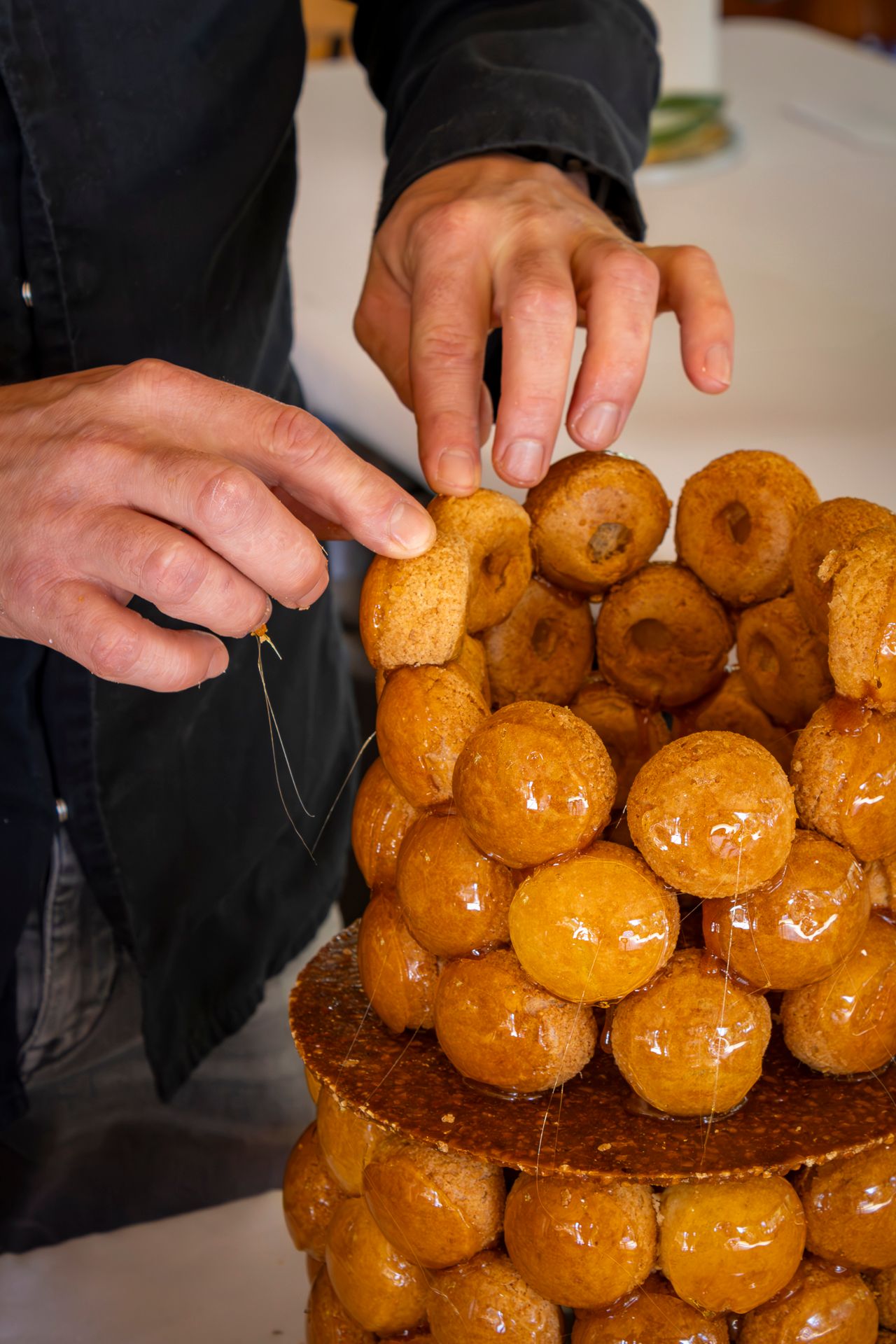 Hands arranging golden brown croquembouche pastry puffs into a cone shape on a dark serving plate.