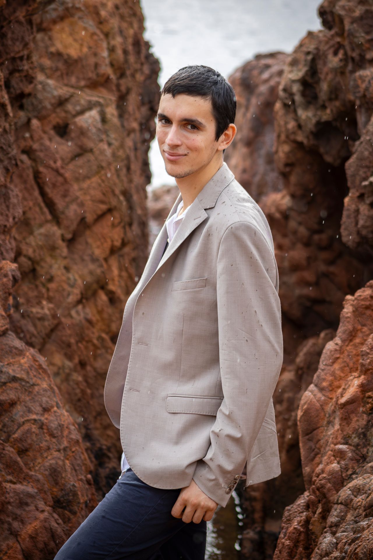 A person in a light gray sweater poses against red rock formations in an outdoor setting.