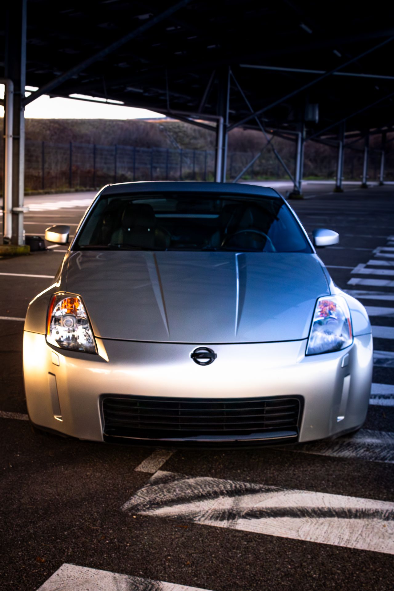 Front view of a silver Nissan 350Z sports car illuminated at night showing its distinctive headlights and grille design.
