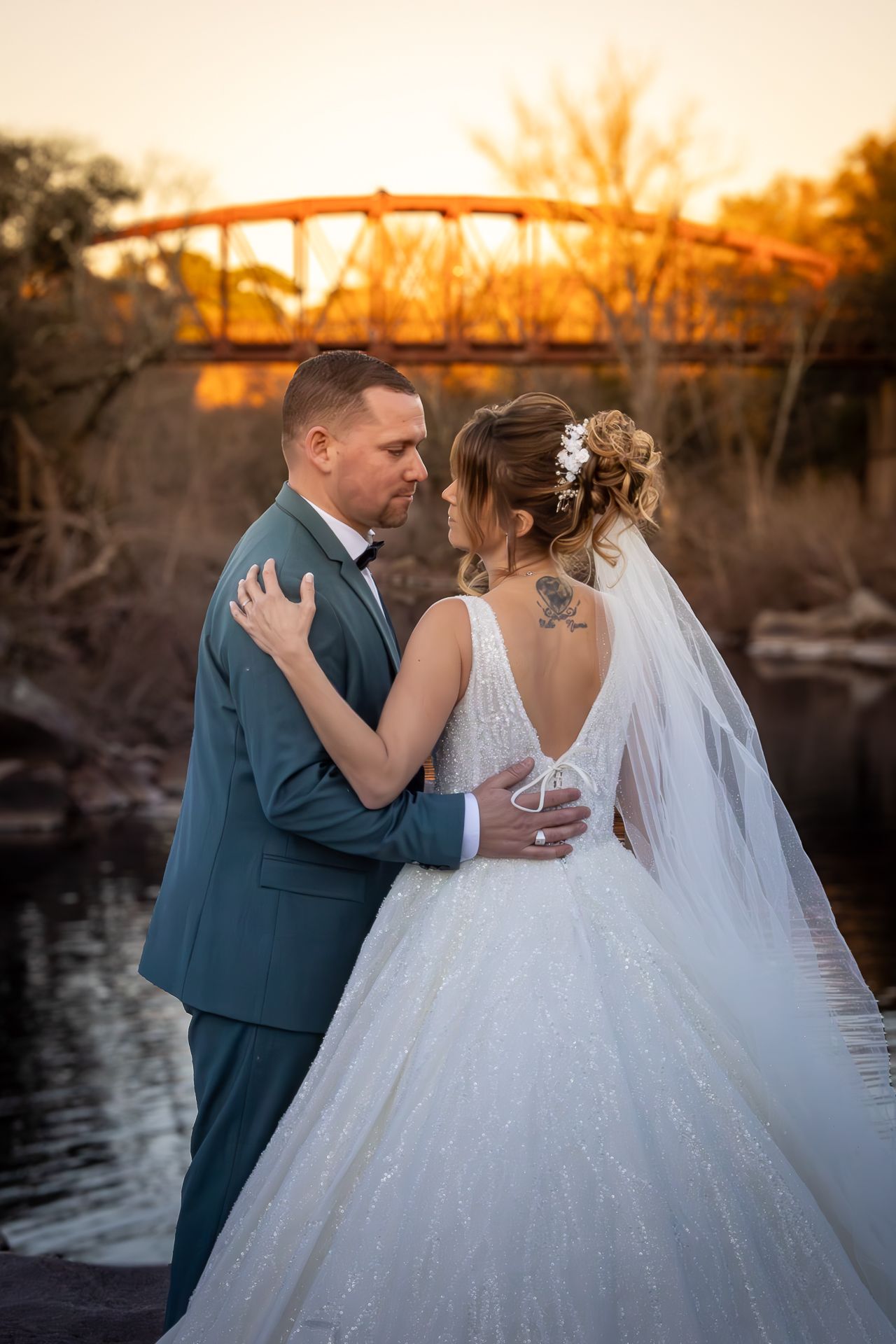 A romantic sunset wedding photoshoot by the water with a couple in formal attire sharing intimate moments.