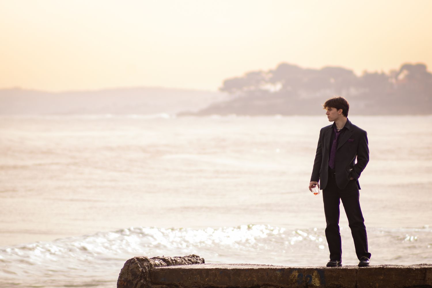 A couple walks along a misty beach at sunset with waves crashing against the shore in the background.
