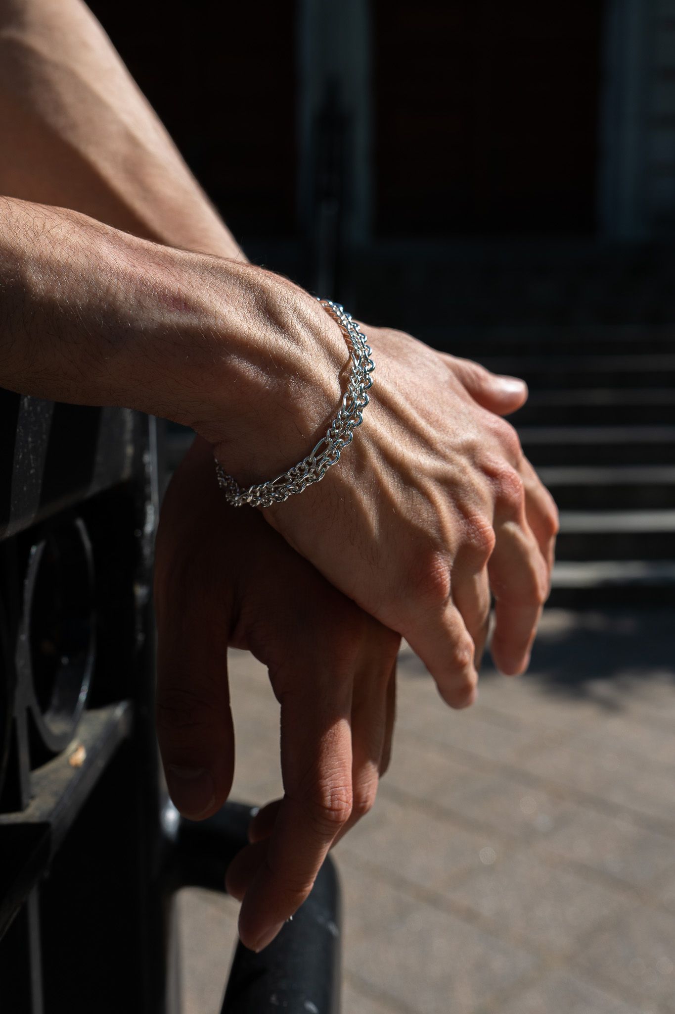 Close-up of hands wearing a silver chain bracelet against a dark background.