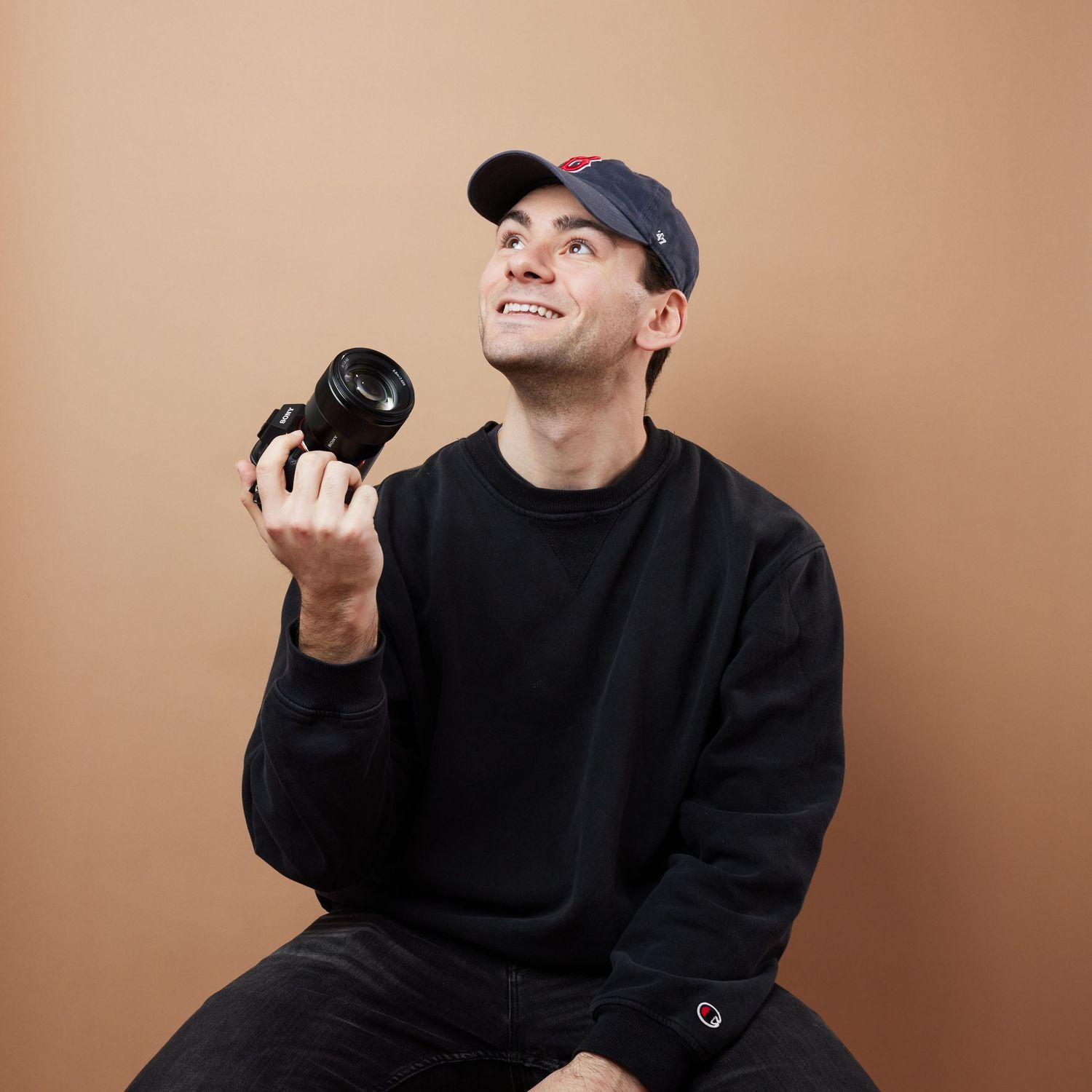 Person in black sweater and baseball cap making expressive gestures against beige background in photo series.