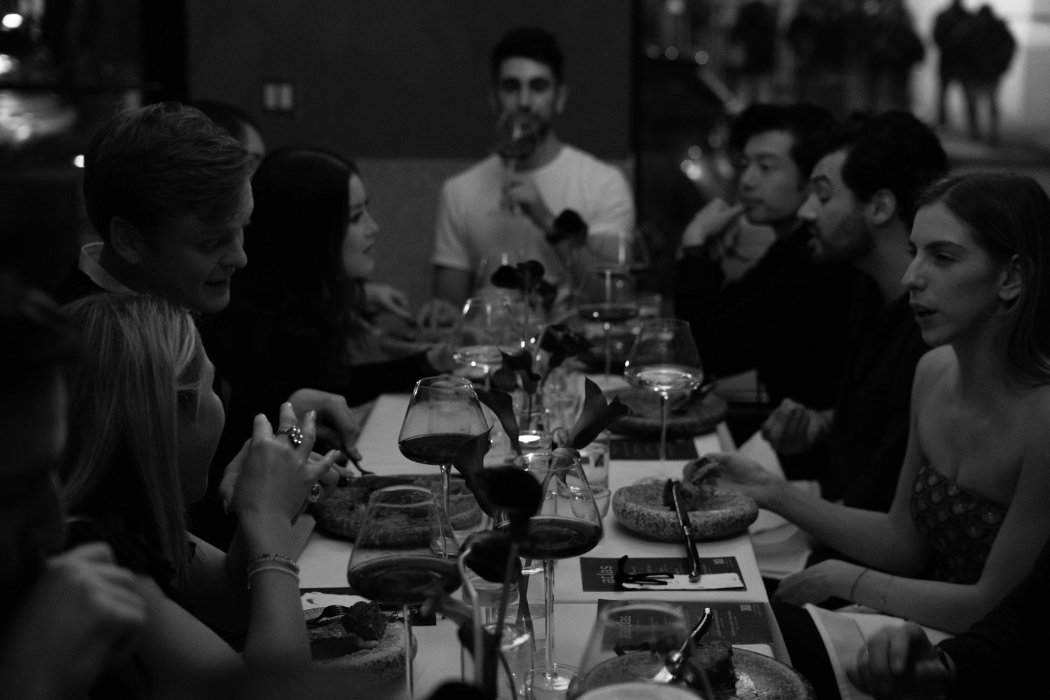 A dimly lit dinner gathering with people seated around a table with glasses and plates.