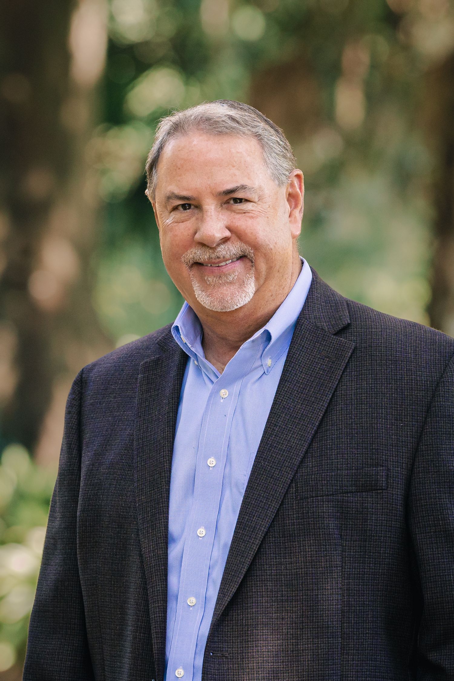 Professional portrait of person in dark suit jacket and light blue button-down shirt.