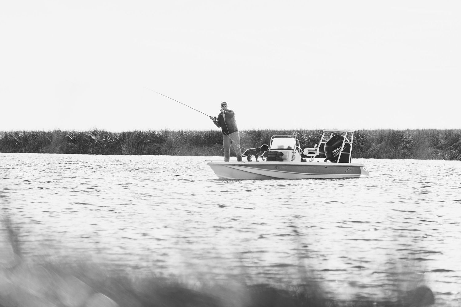 Distant boats fishing on calm waters with a forested shoreline in the background.