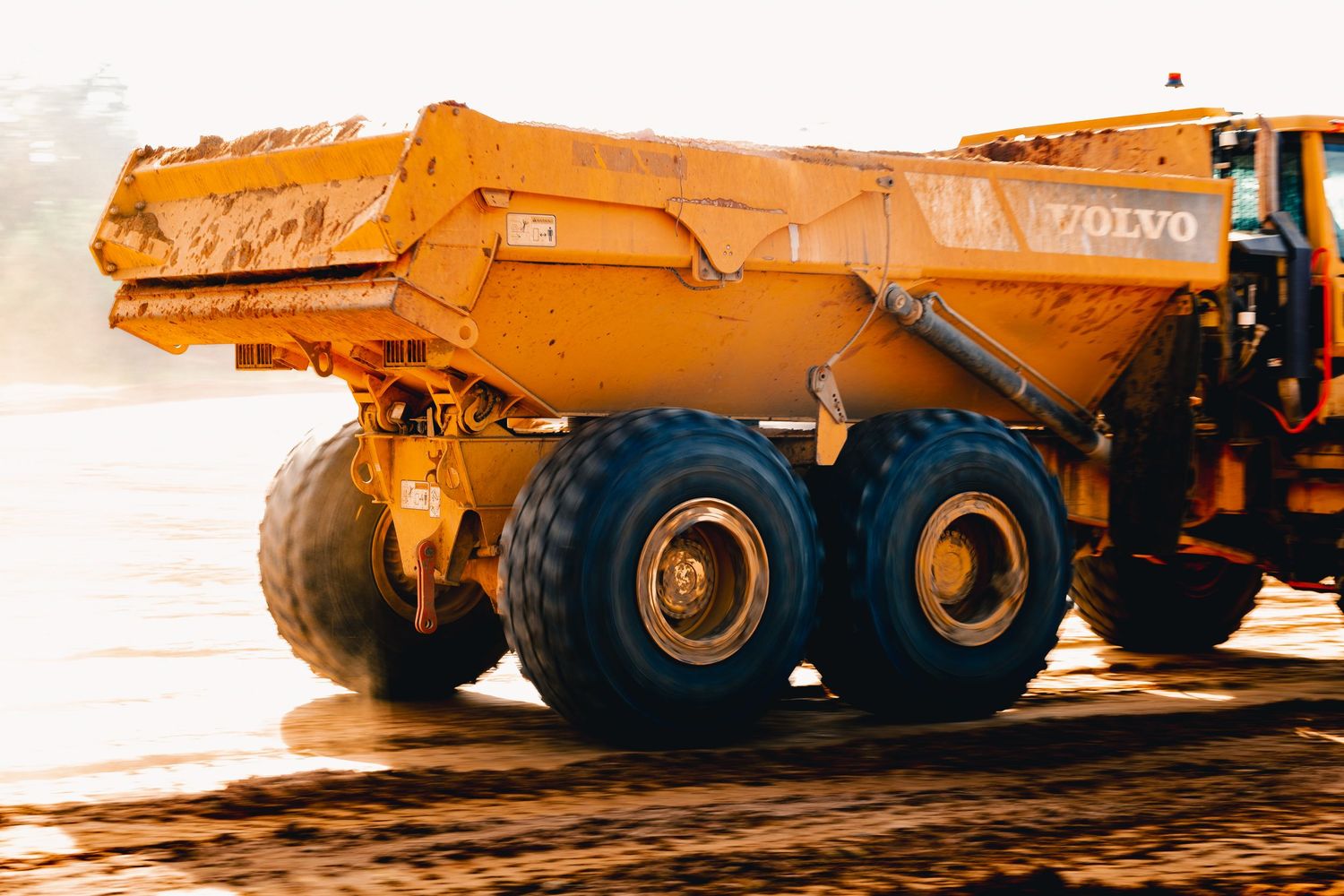 Close-up of a bright orange industrial dump truck with large wheels on a construction site.