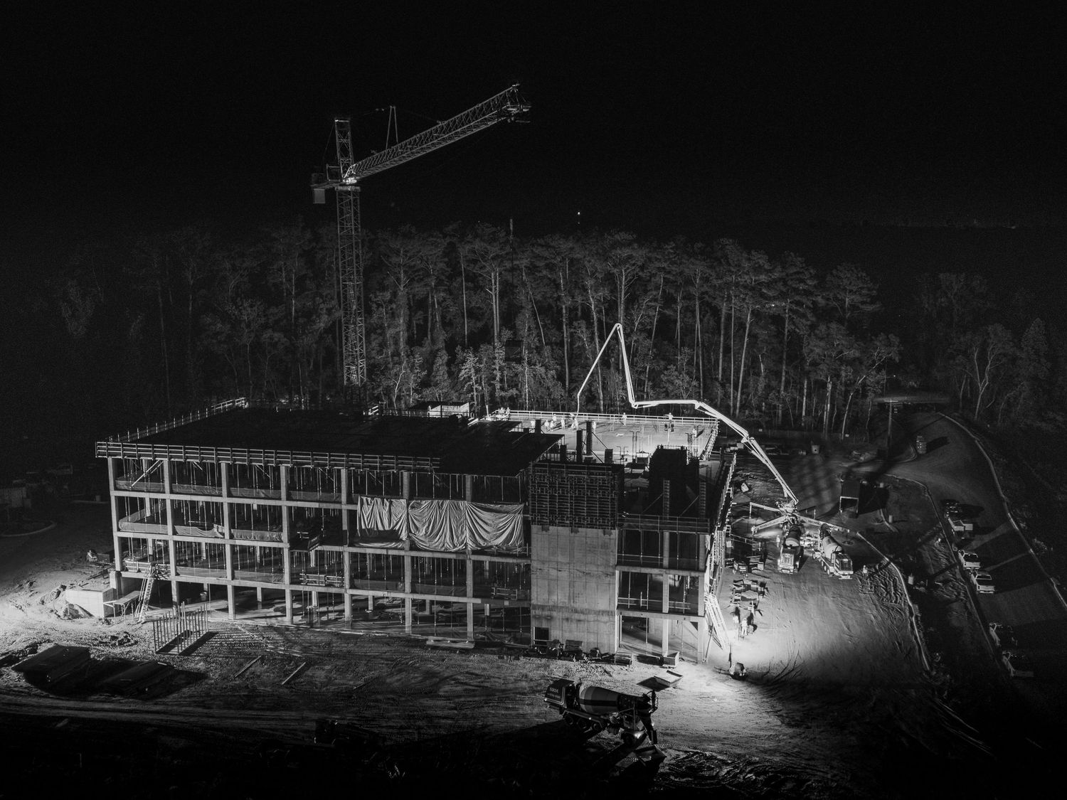 Black and white nighttime construction scene with crane and concrete pumping equipment.