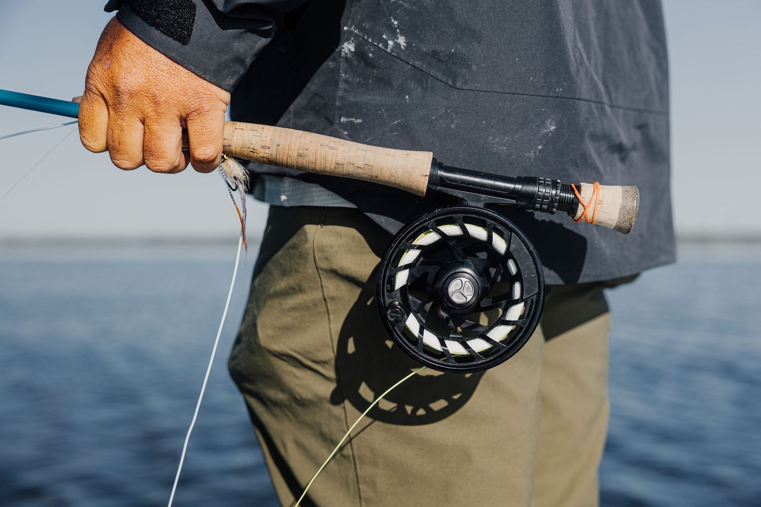 Close-up view of a fly fishing reel and rod against a blue water background.