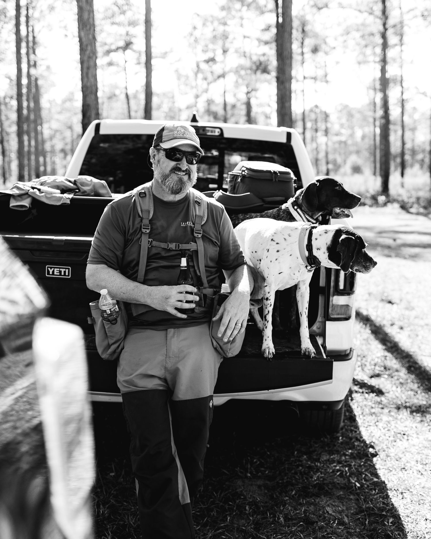 Hunters and their dogs gather near a pickup truck in a black and white forest scene.