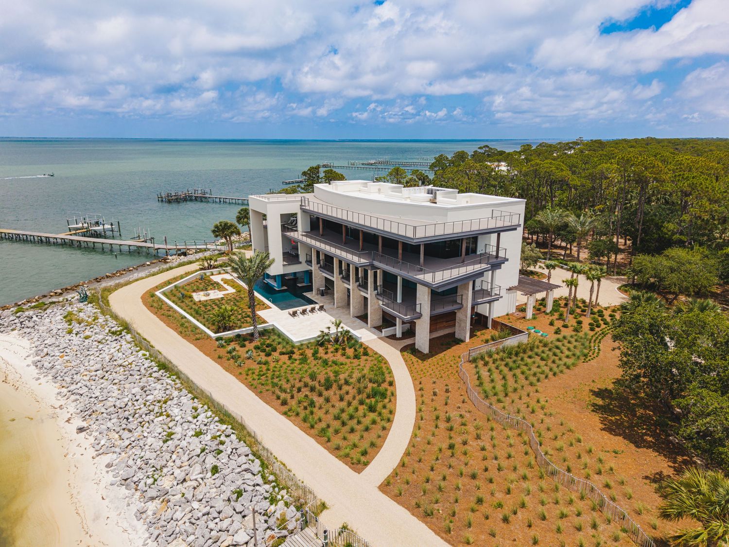 Aerial panoramic views of a modern beachfront property with landscaped gardens and white sandy shoreline.