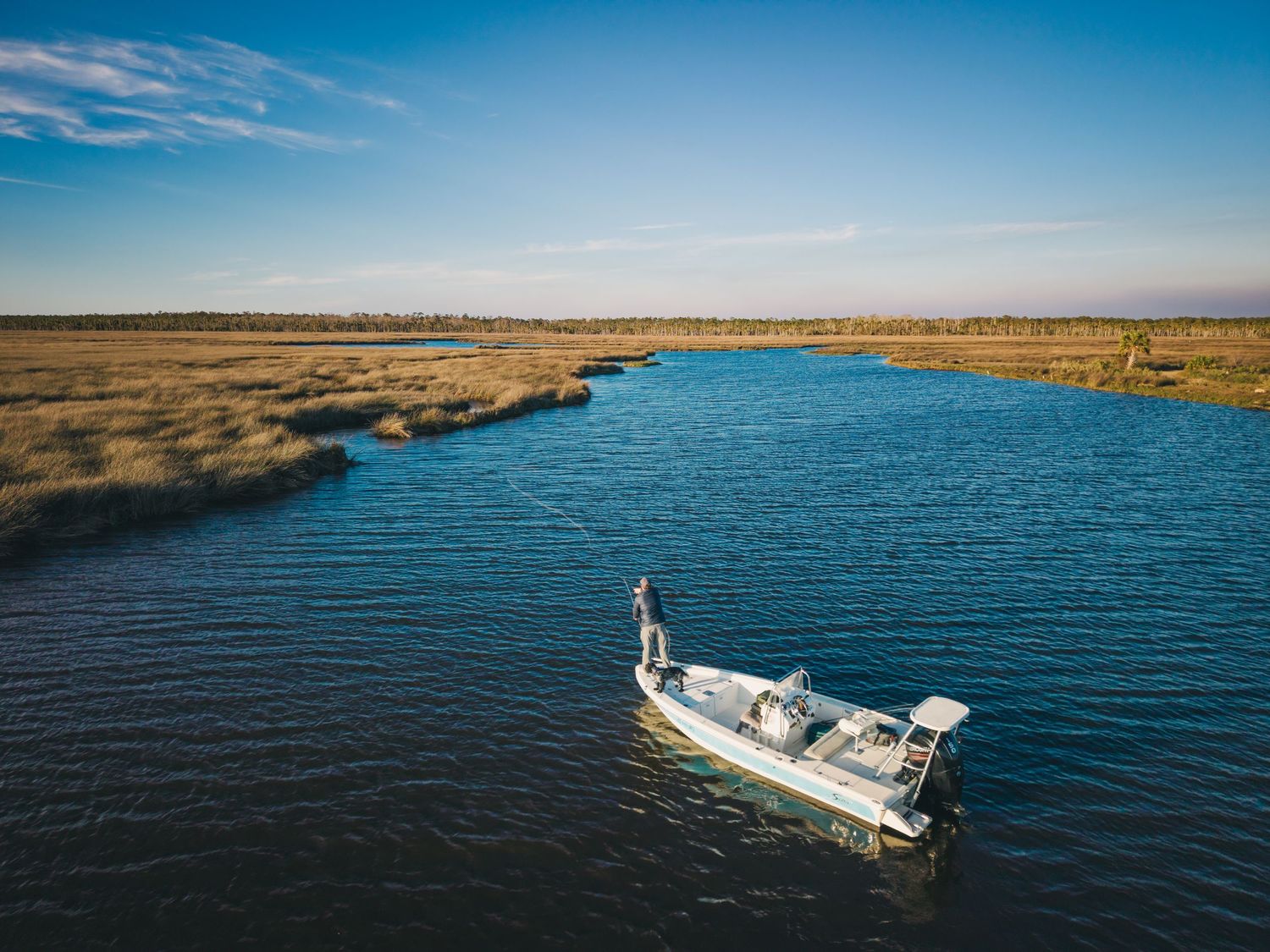 Boats cruise across blue waters near coastal marshland on a clear day.