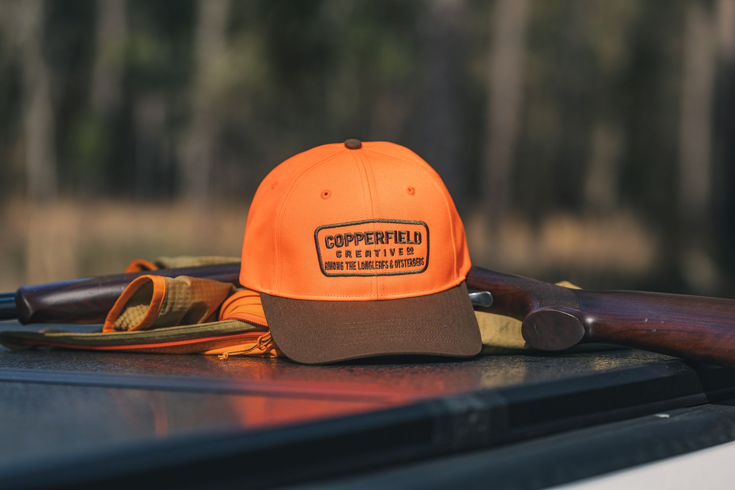 Orange and brown trucker cap with Copper River logo rests on dashboard with fishing gear in background.