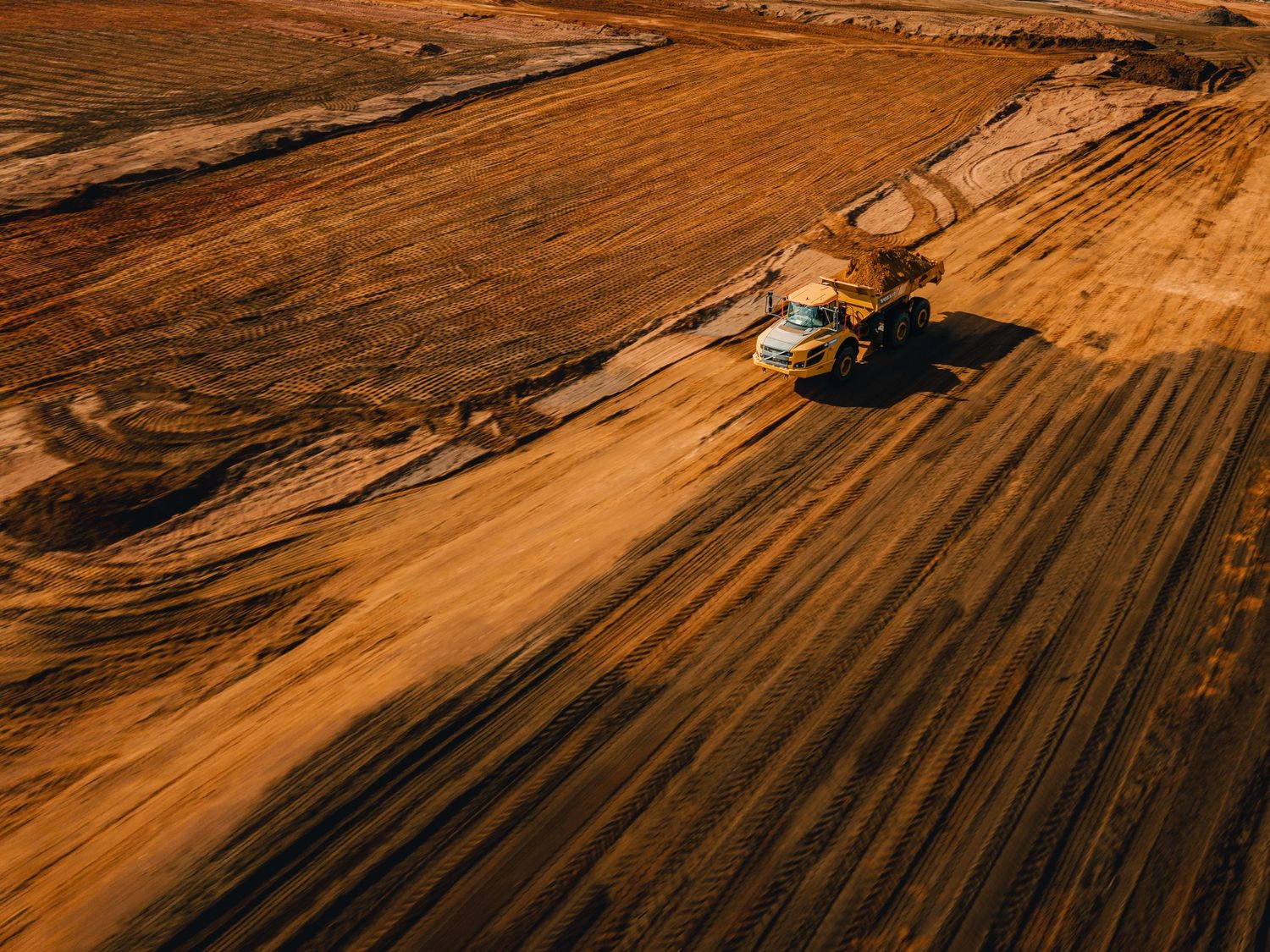 Aerial drone shot of agricultural fields with tractor tracks at sunset creating geometric patterns.