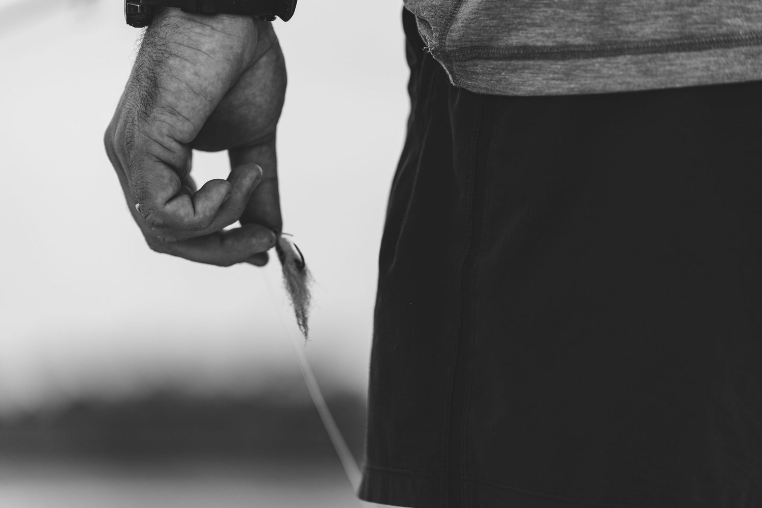 Black and white close-up of hand holding fishing line against light background.