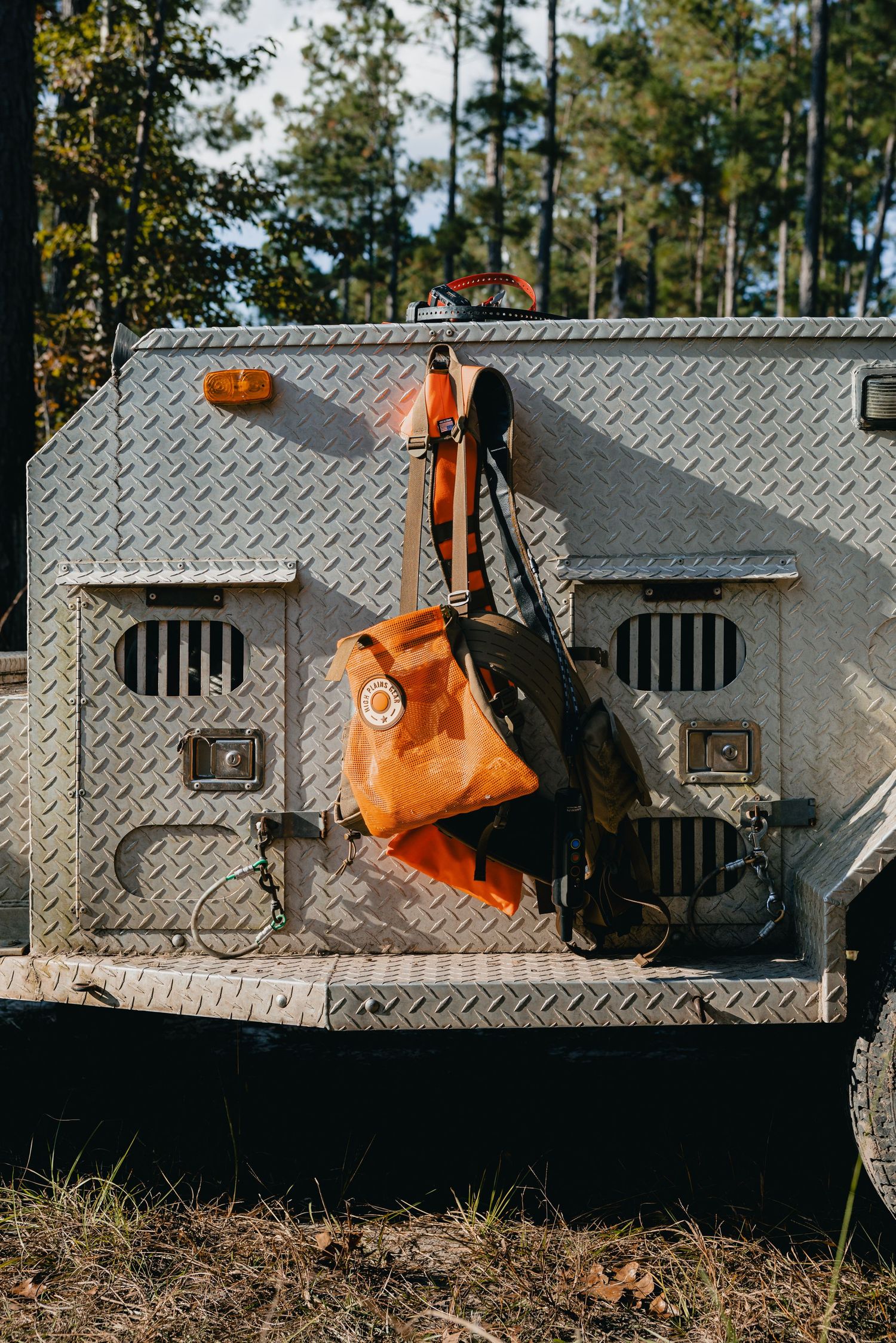 Orange backpack and gear hanging on the back of a rugged aluminum diamond plate off-road vehicle in a forest.