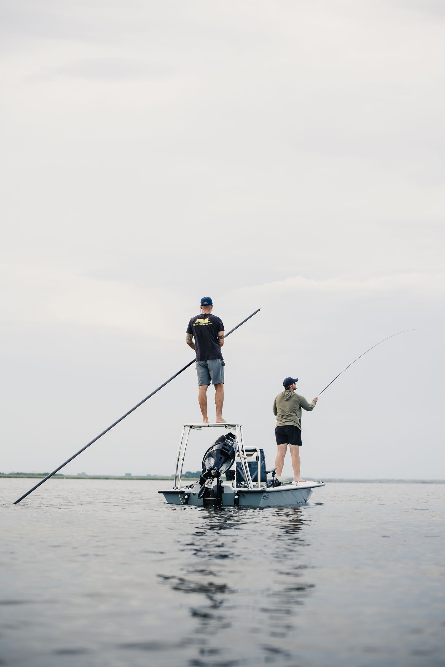 Two anglers fishing from elevated platform on small boat in calm waters.