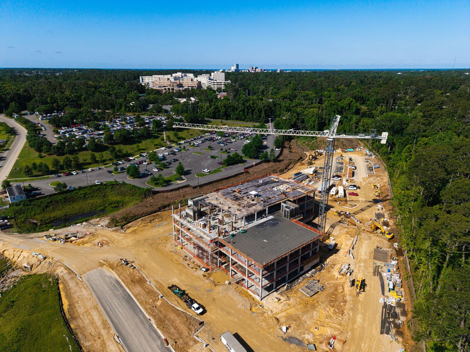 Aerial view of a multi-story building under construction surrounded by forest and parking areas.