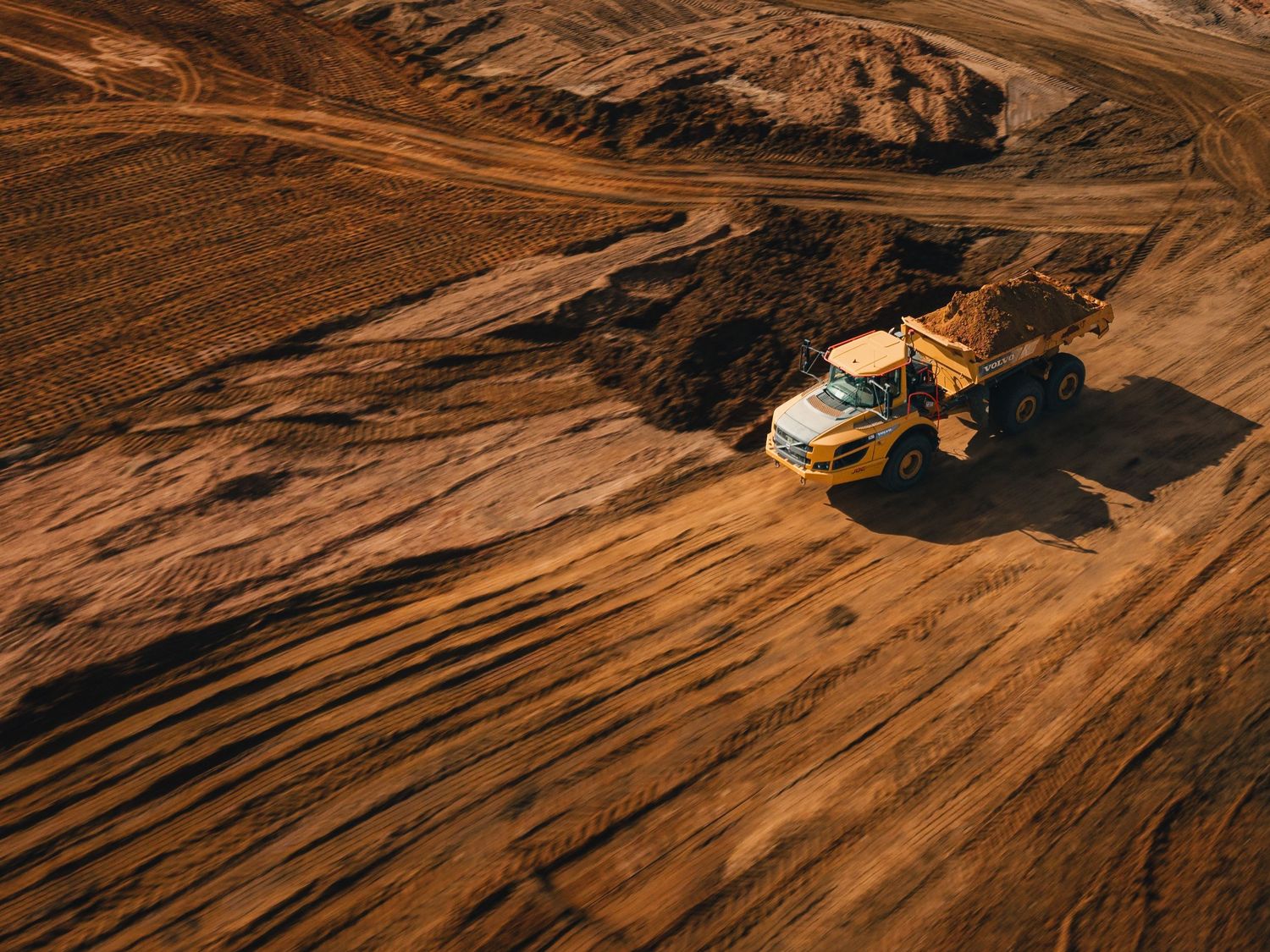 Aerial drone footage shows a mountain biker riding down a steep desert trail with dramatic shadows and ridges.