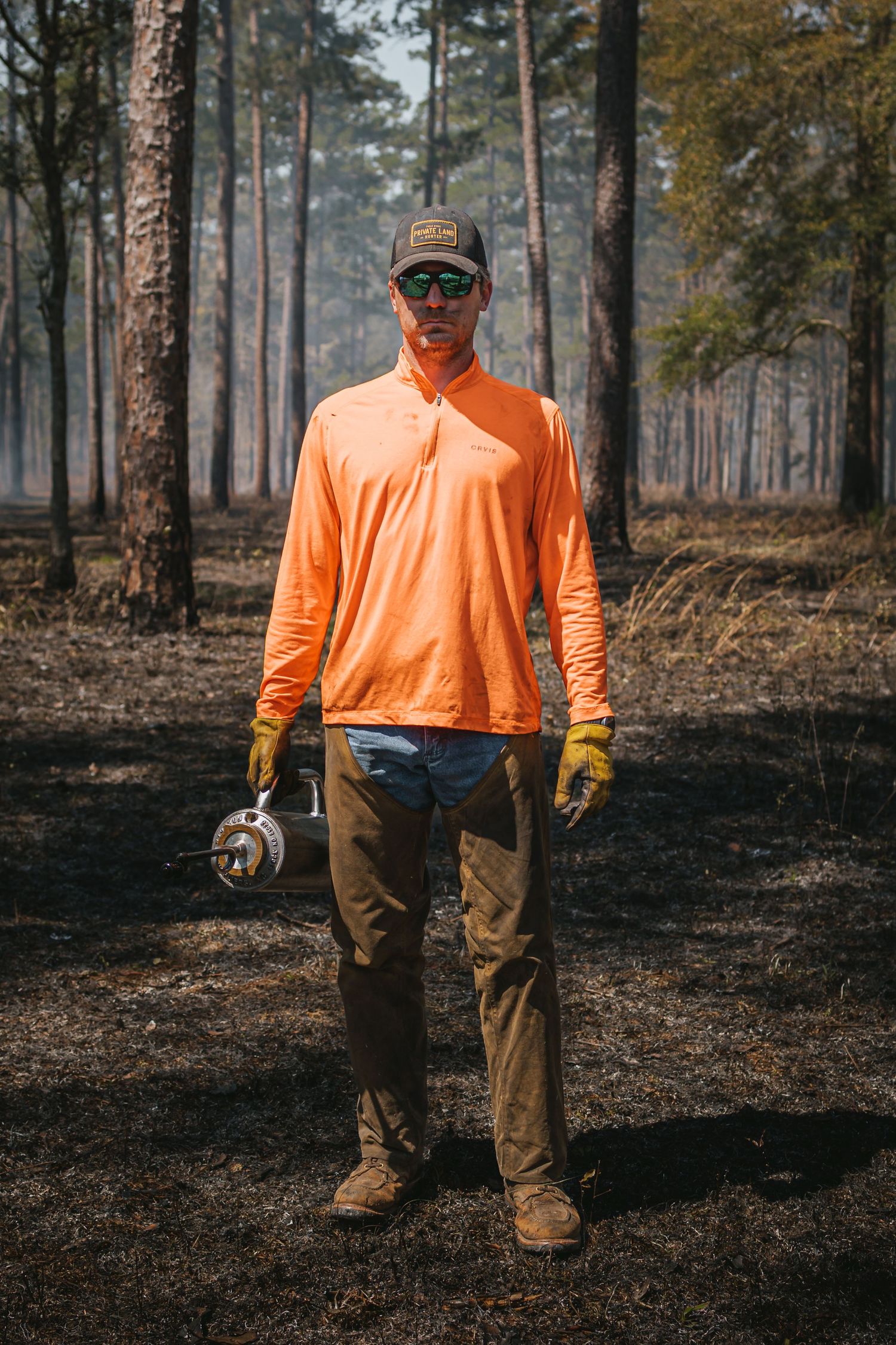 Forest worker in orange safety gear standing on burned ground after prescribed fire.