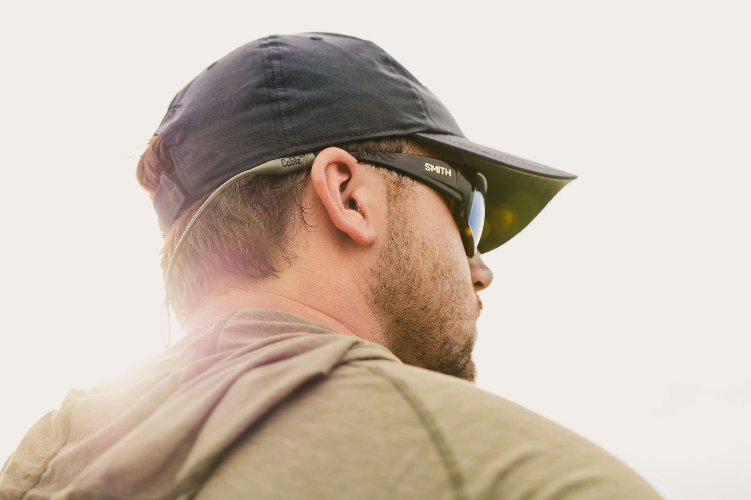 Side view of angler wearing cap and sunglasses against light background.