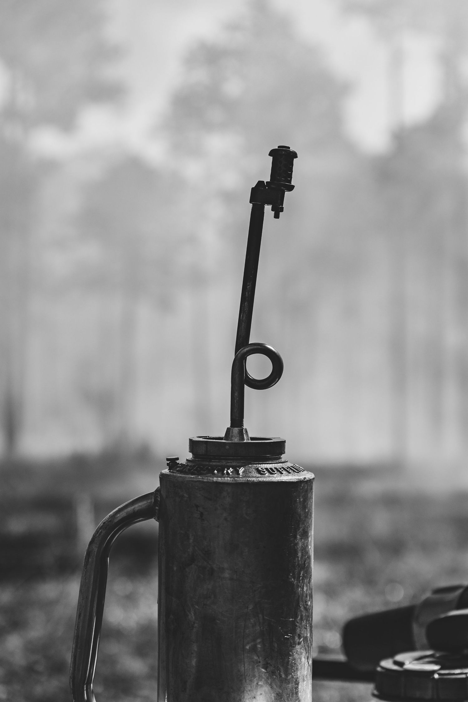 Black and white image of a vintage drip torch silhouetted against a misty forest background.
