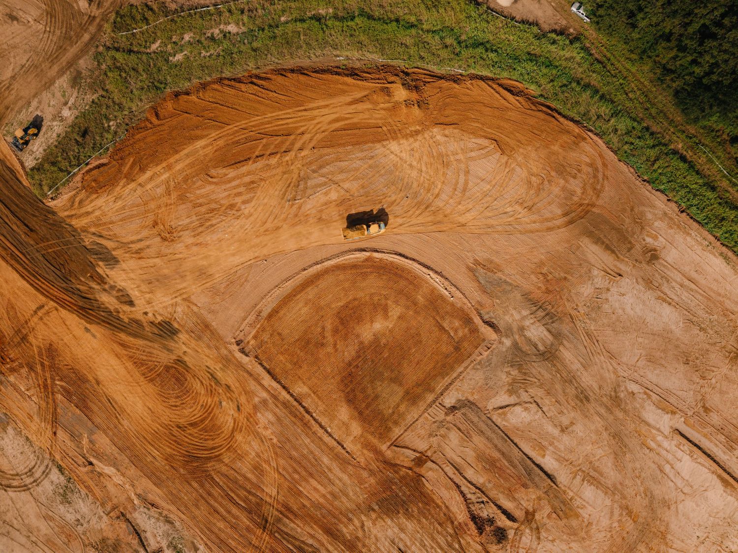 Aerial drone shot of earthmoving equipment creating patterns in a large dirt excavation site.