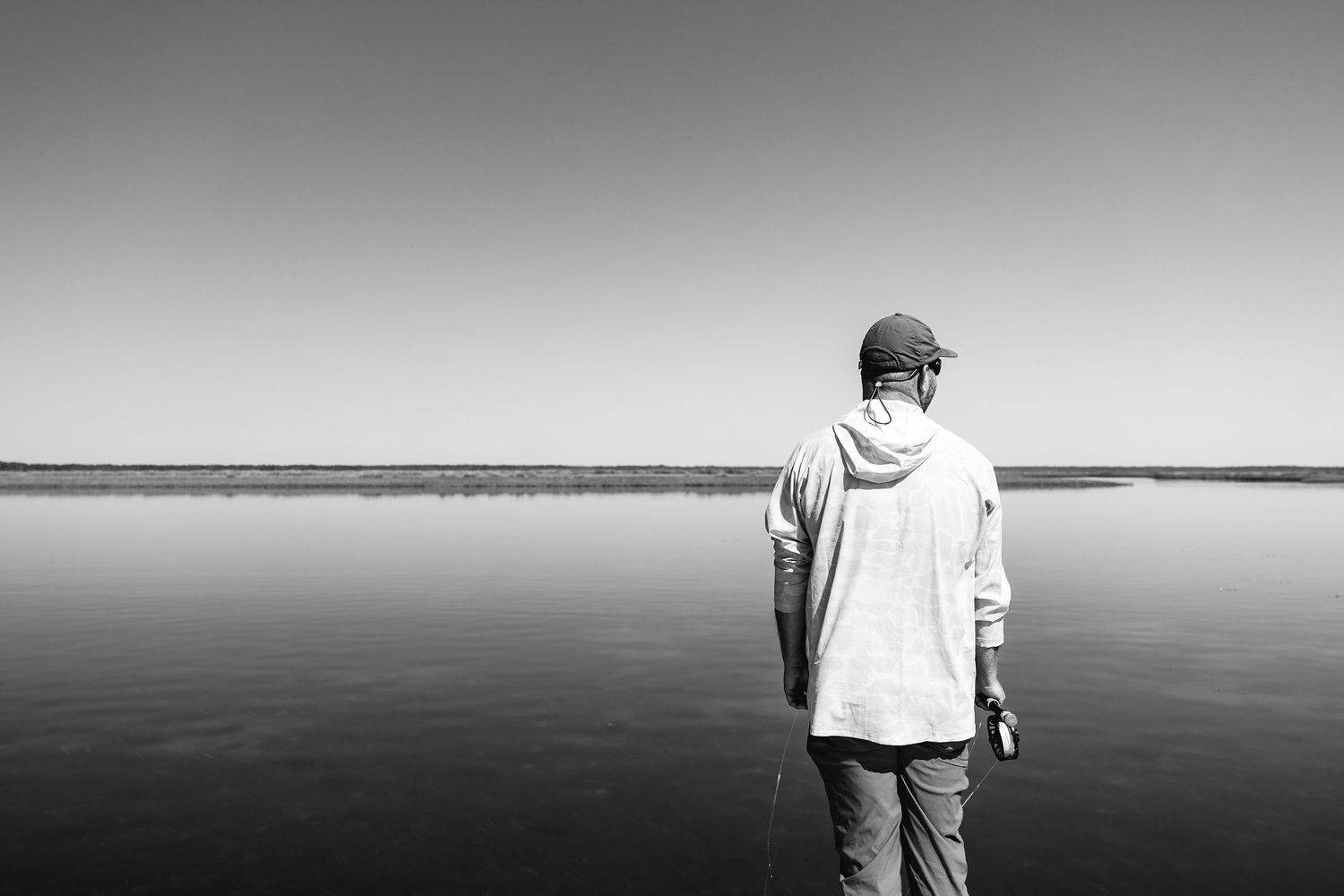 Distant view of angler standing on calm water surface during sunset.