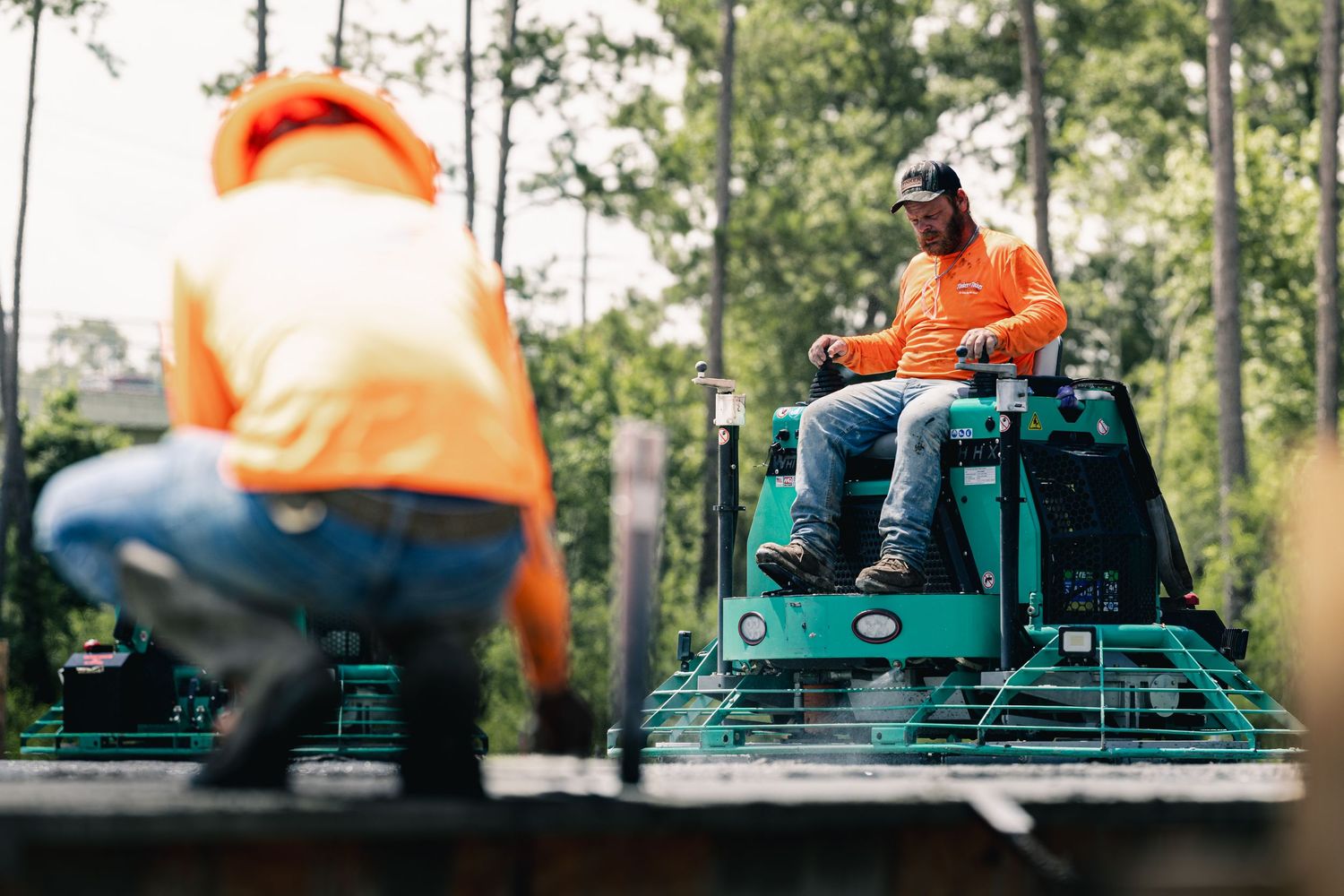 Construction workers operate concrete power trowel machines to smooth freshly poured concrete on a job site.