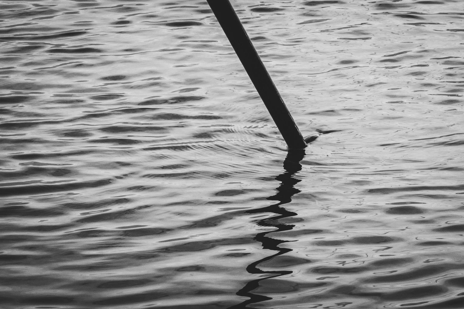 Minimalist black and white photo of a fishing rod tip reflecting in rippling water.