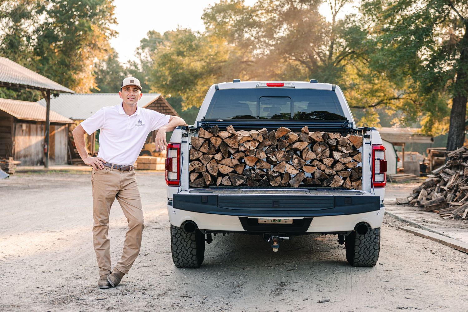 Pickup truck loaded with firewood and person standing beside it in casual attire.