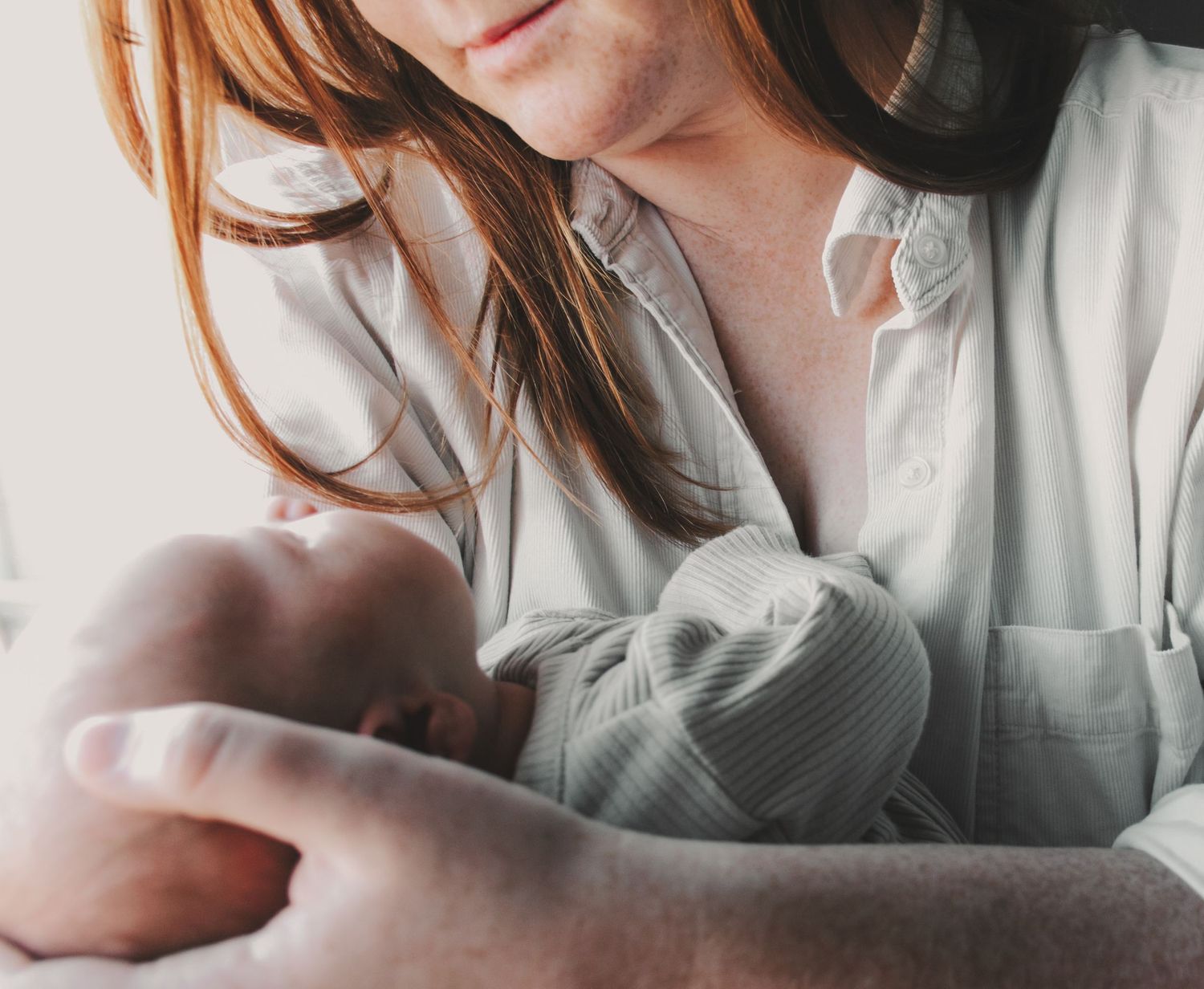 A gentle close-up of someone holding a newborn baby wrapped in a gray hat.